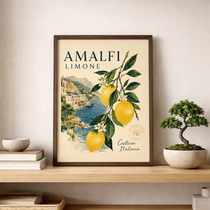 Amalfi Coast lemon poster in a wooden frame placed on a shelf beside a small bonsai plant and neutral home decor. The print shows yellow lemons, green leaves and an Italian seaside village, making it a fresh Mediterranean wall art piece for kitchen, dining or living spaces.
