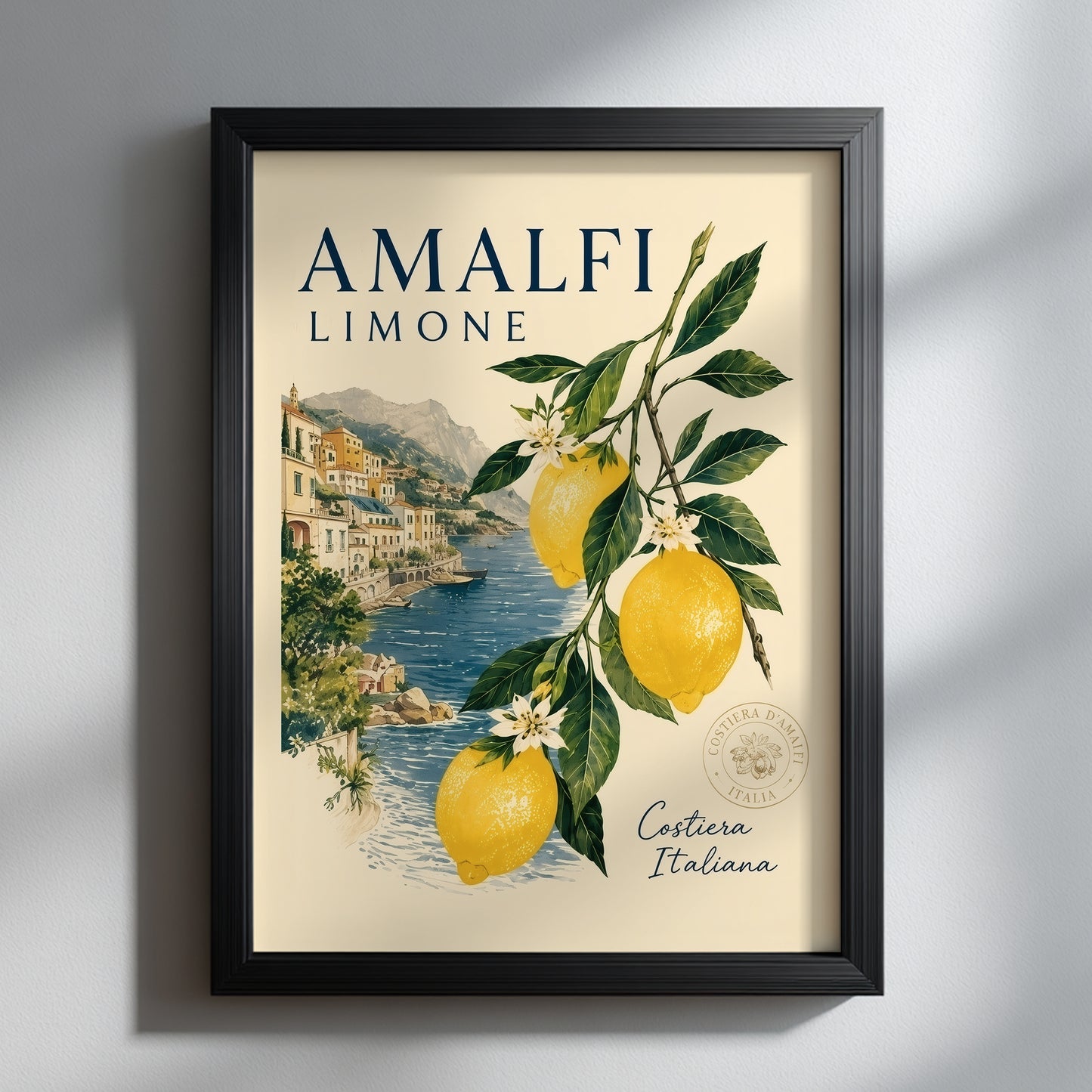 lack framed Amalfi Coast lemon print hanging on a clean light wall with soft shadow. The Italian travel poster shows bright yellow lemons, green leaves and a coastal village by the sea, giving a fresh Mediterranean summer look for modern kitchen or living room decor.