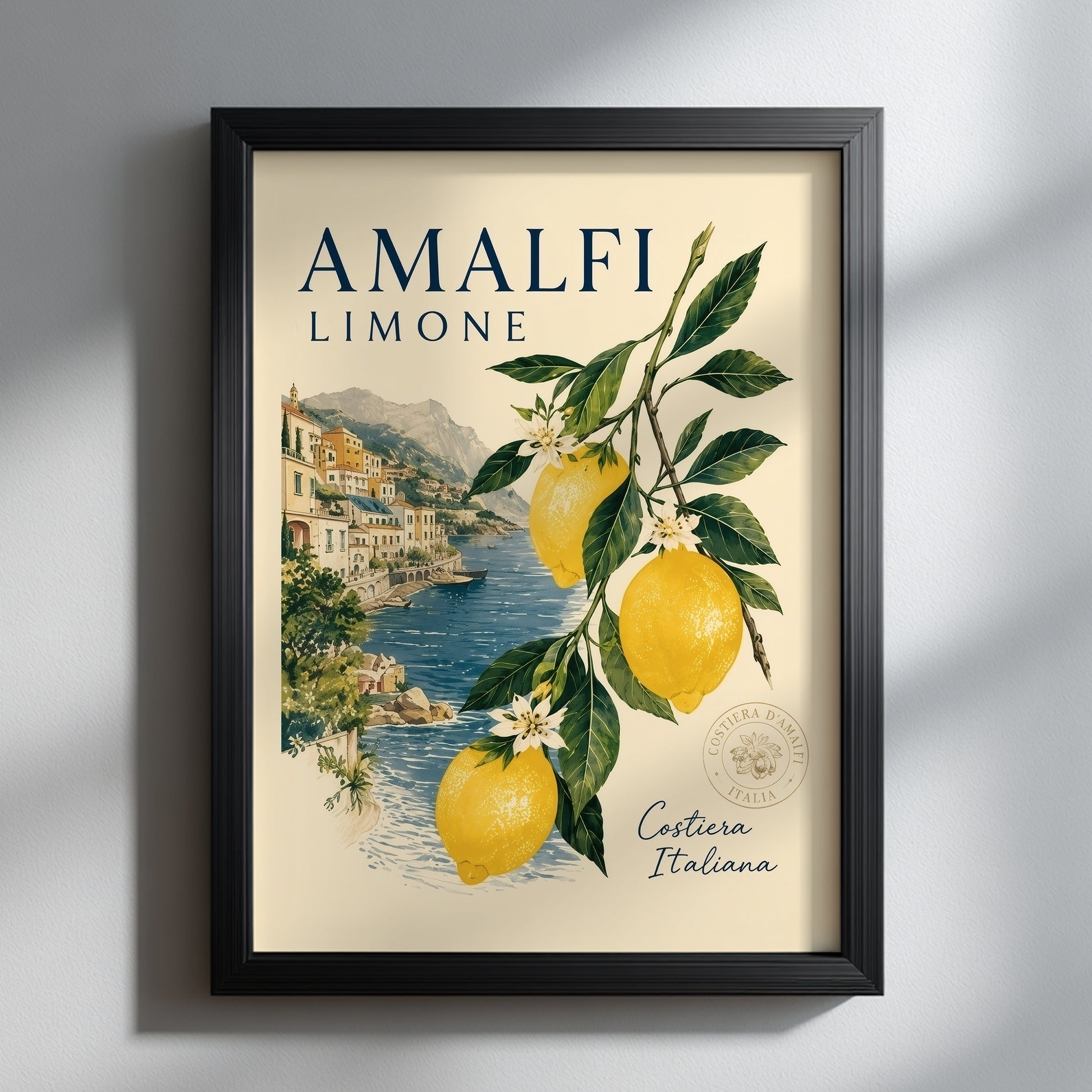lack framed Amalfi Coast lemon print hanging on a clean light wall with soft shadow. The Italian travel poster shows bright yellow lemons, green leaves and a coastal village by the sea, giving a fresh Mediterranean summer look for modern kitchen or living room decor.