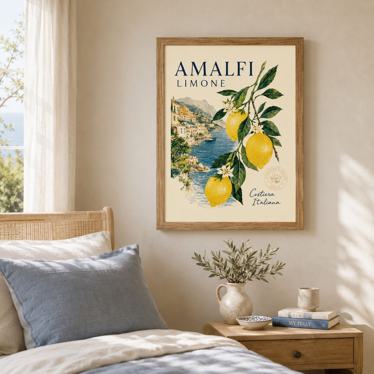 Framed Amalfi Coast lemon poster displayed above a bedside table in a soft neutral bedroom. The artwork shows yellow lemons, green leaves, white blossom flowers and an Italian coastal village scene, styled as Mediterranean travel wall art for calm summer home decor.