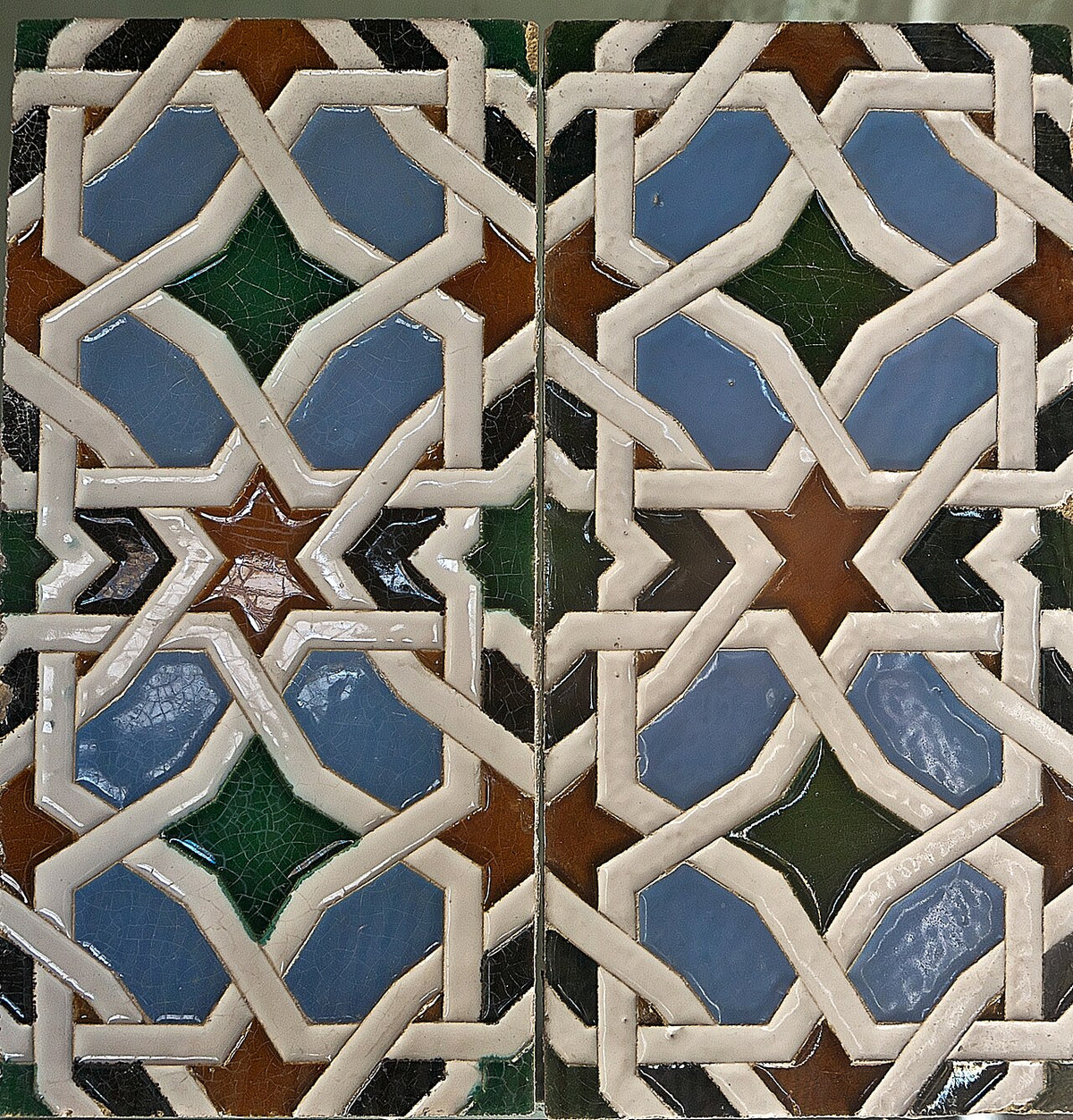 Two square ceramic tiles featuring an intricate geometric Islamic star pattern with blue, green, brown, and white glazed sections.

Jl FilpoC, CC BY-SA 4.0 <https://creativecommons.org/licenses/by-sa/4.0>, via Wikimedia Commons