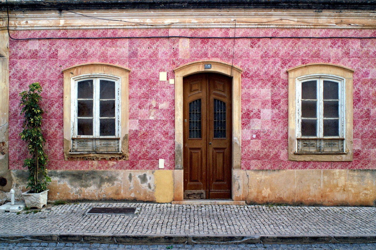 Historic pink tiled building façade with a traditional wooden door, white-framed windows and patterned cobbled pavement in Portugal.