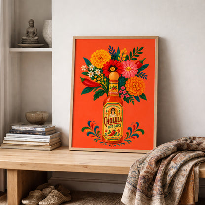 Colourful Mexican spicy sauce art print leaning on a wooden shelf beside stacked books, pottery and a textured woven throw, creating a warm kitchen or café styling scene with neutral walls.