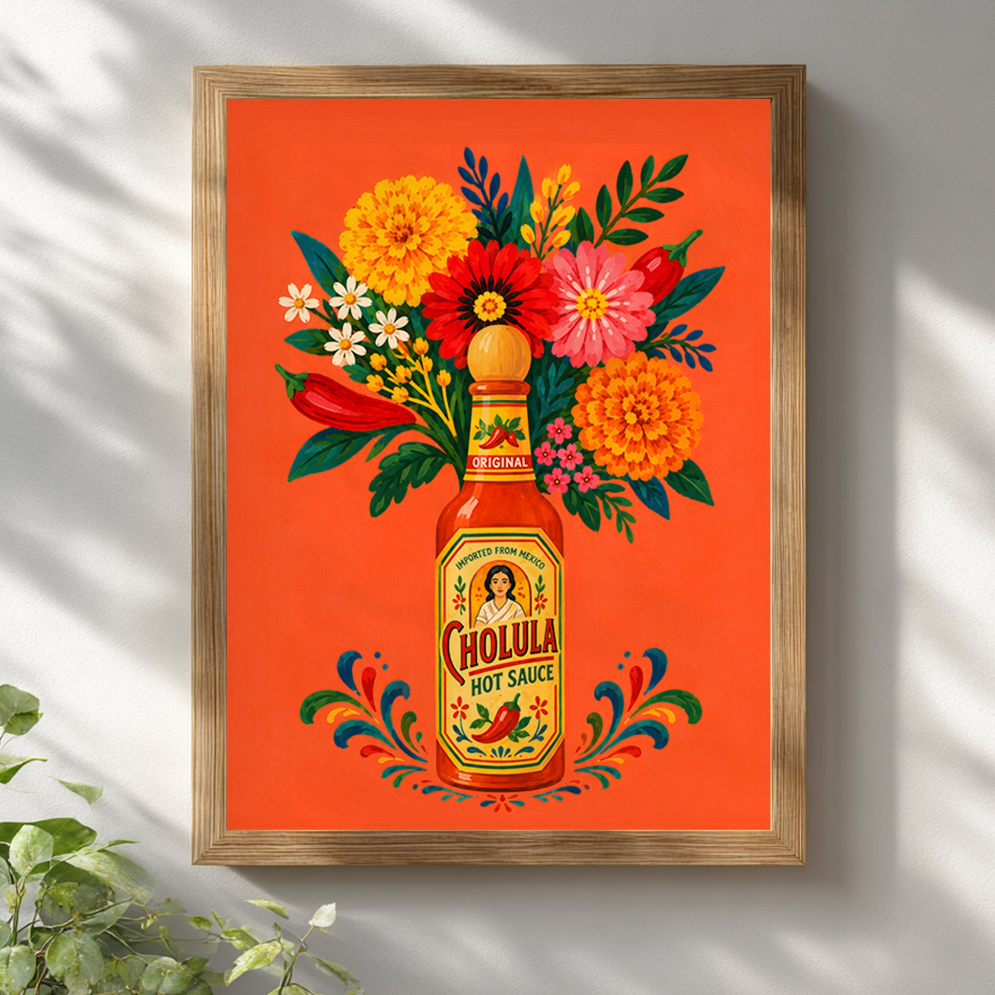 Mexican spicy sauce bottle and floral art print displayed in a light wooden frame on a white wall, with soft leaf shadows and natural daylight emphasising the orange, yellow, red, pink and green palette.