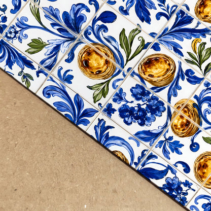 Close-up angled view of Portuguese azulejo wall art showing blue floral tile patterns, green leaves and golden pastel de nata custard tarts with visible printed detail.