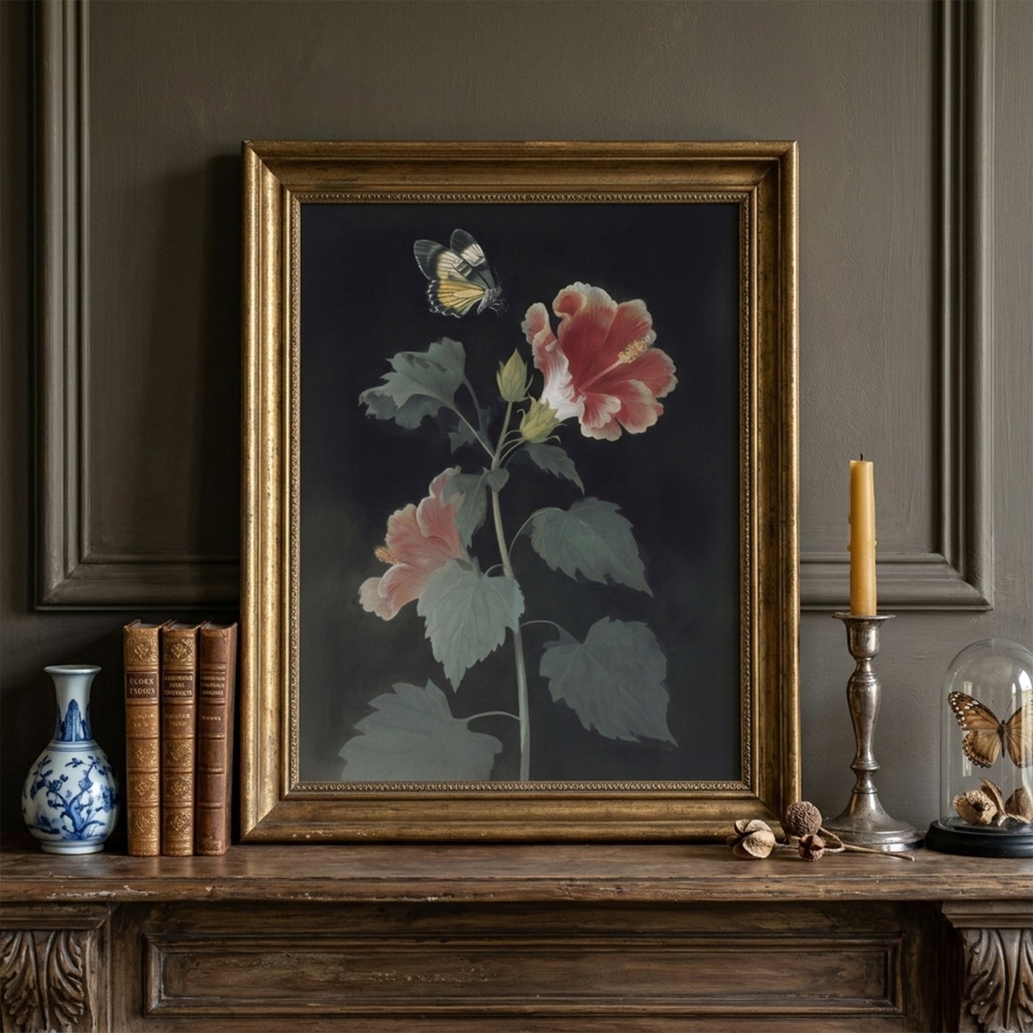 Framed Malaysian hibiscus and Rajah Brooke’s Birdwing butterfly artwork displayed on a mantle with books and decorative objects. The botanical print features red and pink hibiscus flowers with green leaves against a dark background, styled as vintage botanical wall art in a traditional interior setting.