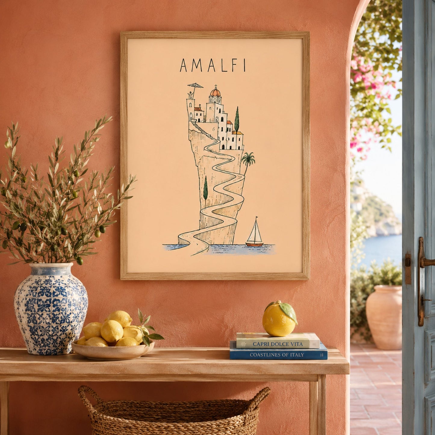 Framed Amalfi Coast travel print displayed above a wooden console against a terracotta wall, styled with a patterned vase, leafy stems and decorative objects.