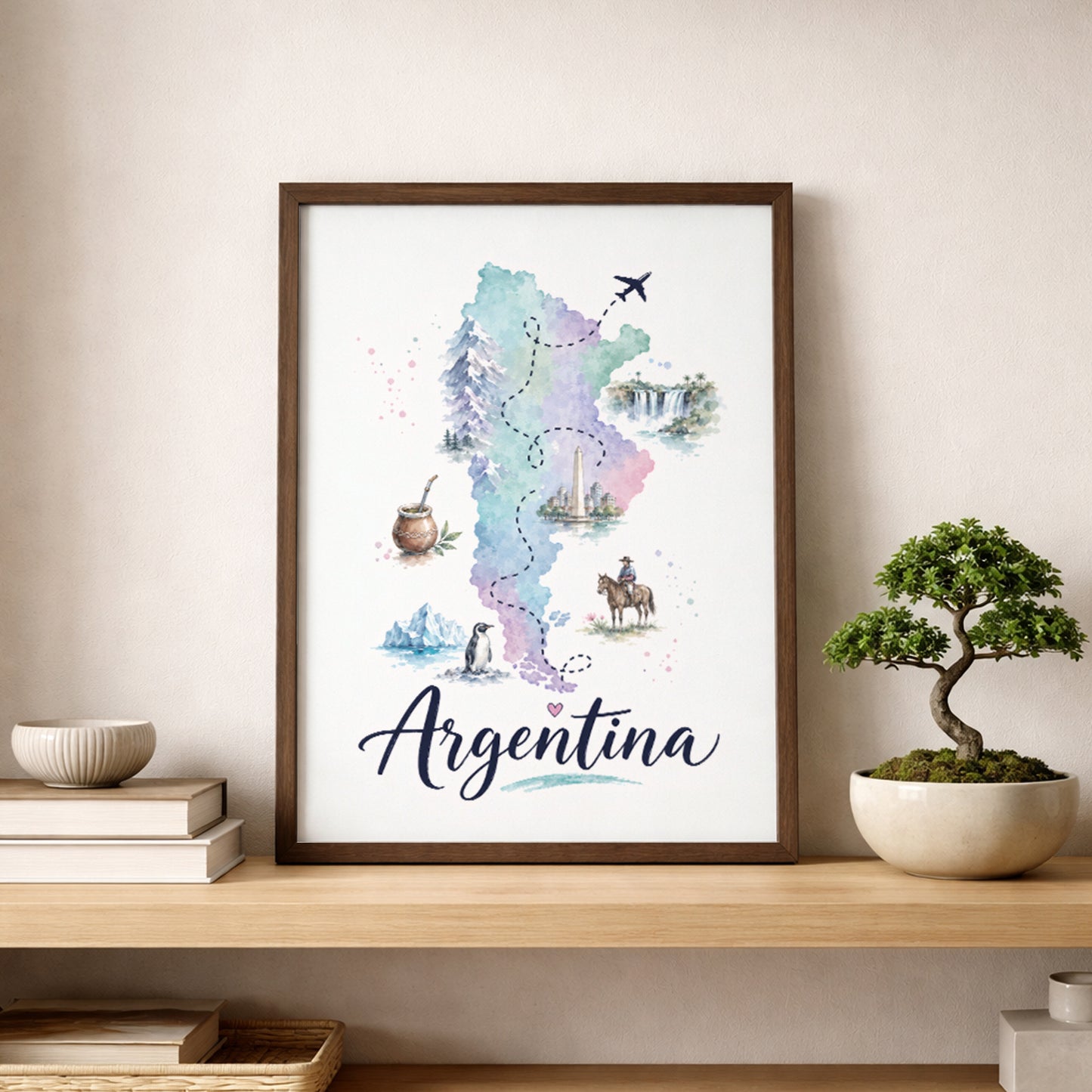 Framed Argentina map wall art resting on a wooden shelf in a calm neutral room. The pastel watercolour map is decorated with small cultural, wildlife and travel illustrations, with large cursive Argentina lettering beneath. A cream sofa, stacked books, ceramic decor and a small bonsai-style plant complete the warm travel-inspired display.