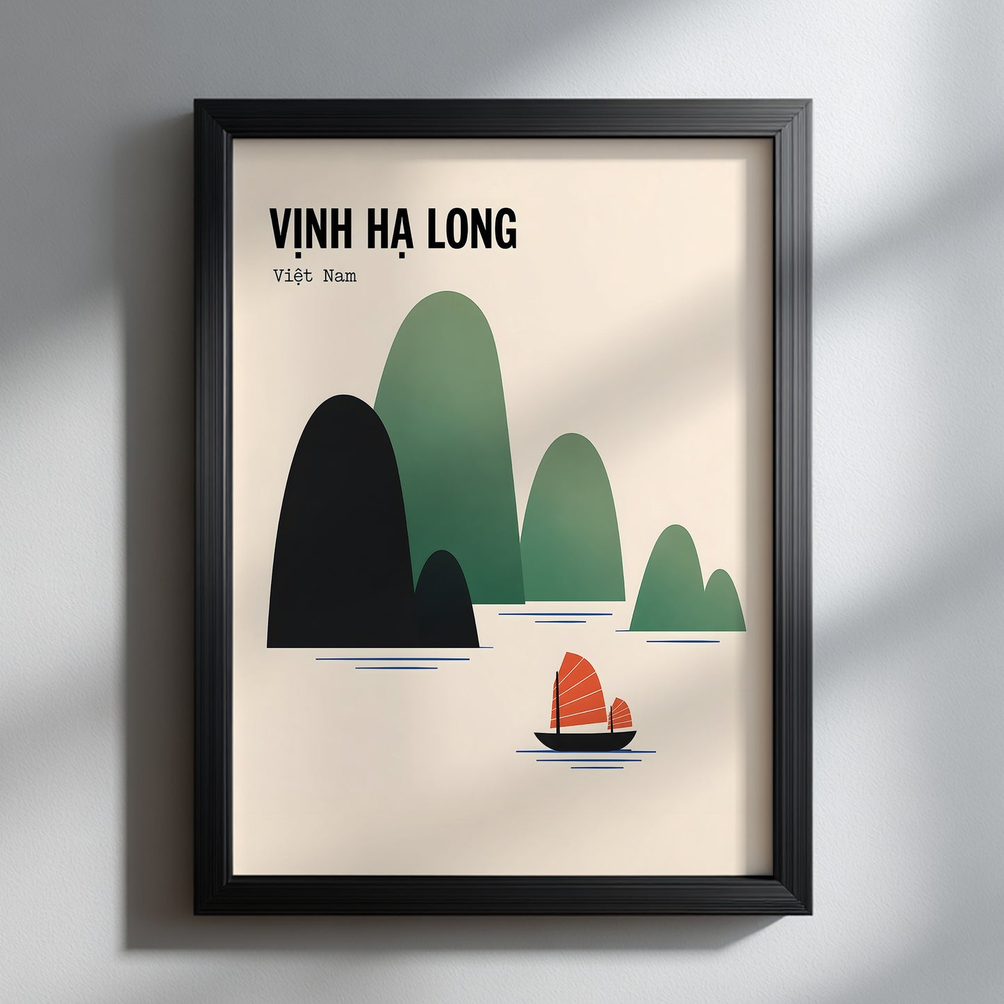Ha Long Bay Vietnam travel poster presented in a slim black frame against a soft grey interior. Window light casts gentle shadows across the wall and surface, while the cream artwork, layered green limestone islands and orange junk boat stand out as clean, modern travel wall art.