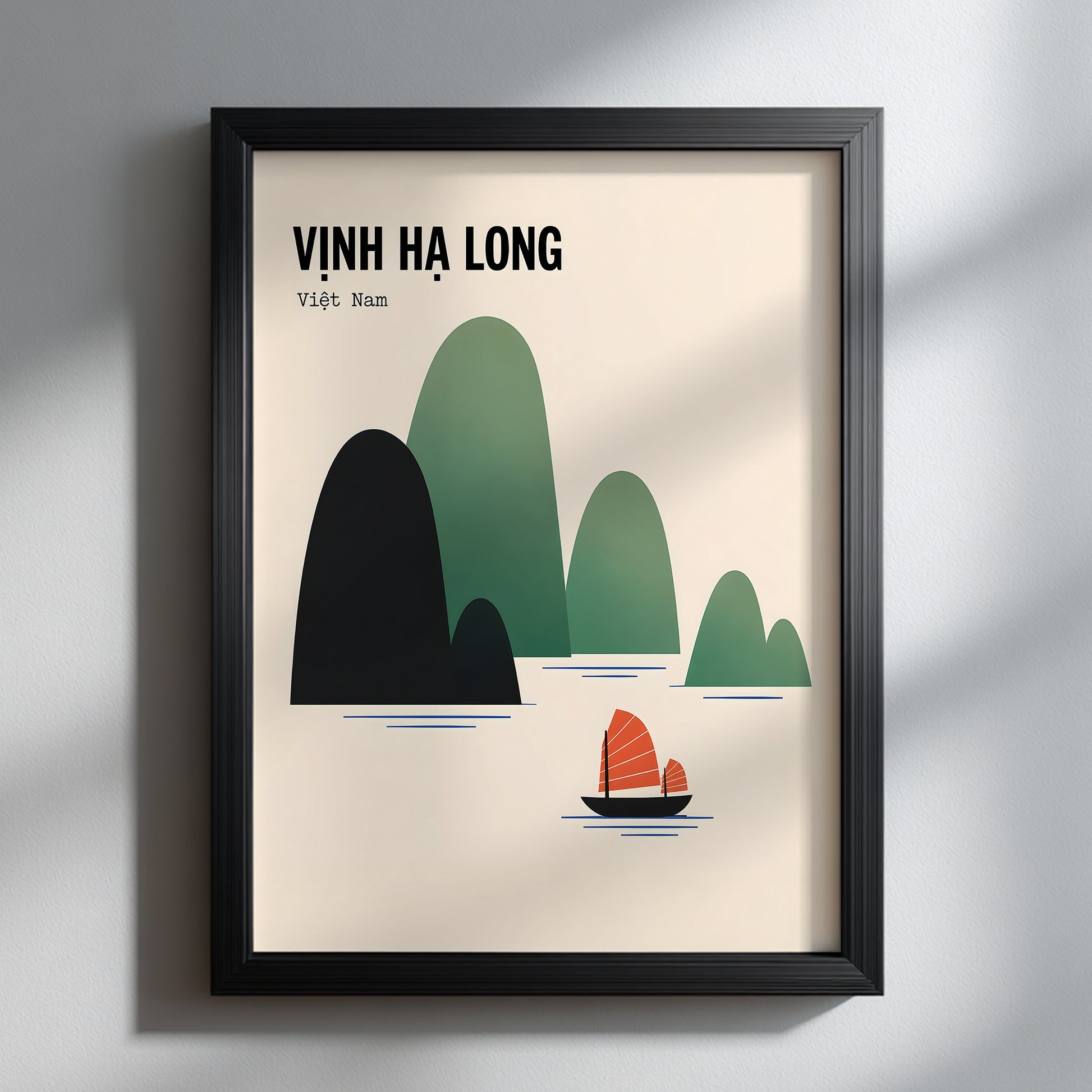 Ha Long Bay Vietnam travel poster presented in a slim black frame against a soft grey interior. Window light casts gentle shadows across the wall and surface, while the cream artwork, layered green limestone islands and orange junk boat stand out as clean, modern travel wall art.