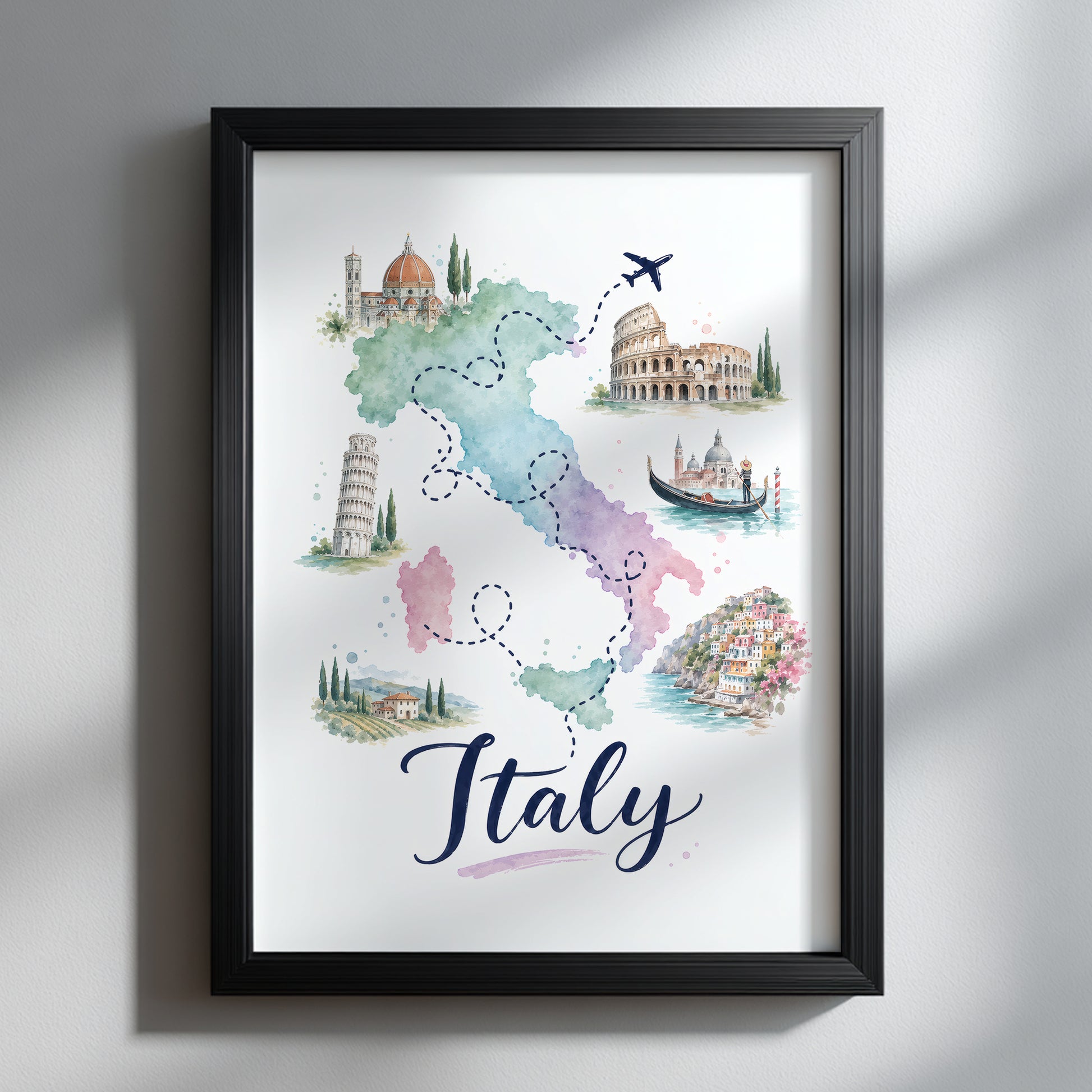 Italy travel map print presented in a slim black frame on a soft grey wall. The pastel watercolour map combines green, pink, blue and purple sections with dotted journey lines, a small aeroplane and illustrated Italian landmarks, while the bold handwritten Italy title makes the artwork stand out in a clean, modern interior.
