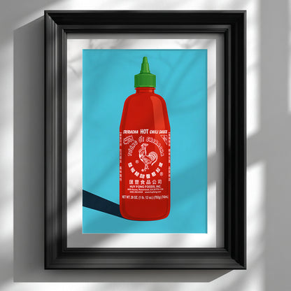 Black framed sriracha poster on a white wall, featuring a bold red hot sauce bottle with a green cap, white rooster label, bright blue background and strong pop art style. A colourful food print for kitchen wall art, dining room decor, cafe walls, restaurant styling or a modern foodie gallery wall.