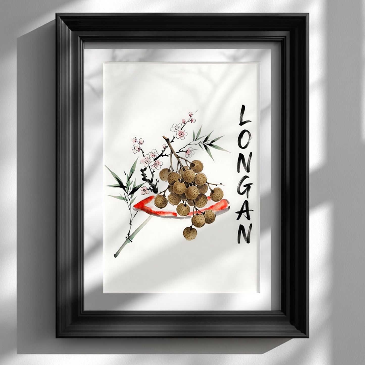 Black framed wall art print showing a minimalist Thai longan watercolour on a white wall. The artwork has brown longan fruit, green bamboo-style leaves, small blossom details and vertical black lettering, styled as Southeast Asia inspired fruit decor for kitchens, dining rooms or calm home interiors.