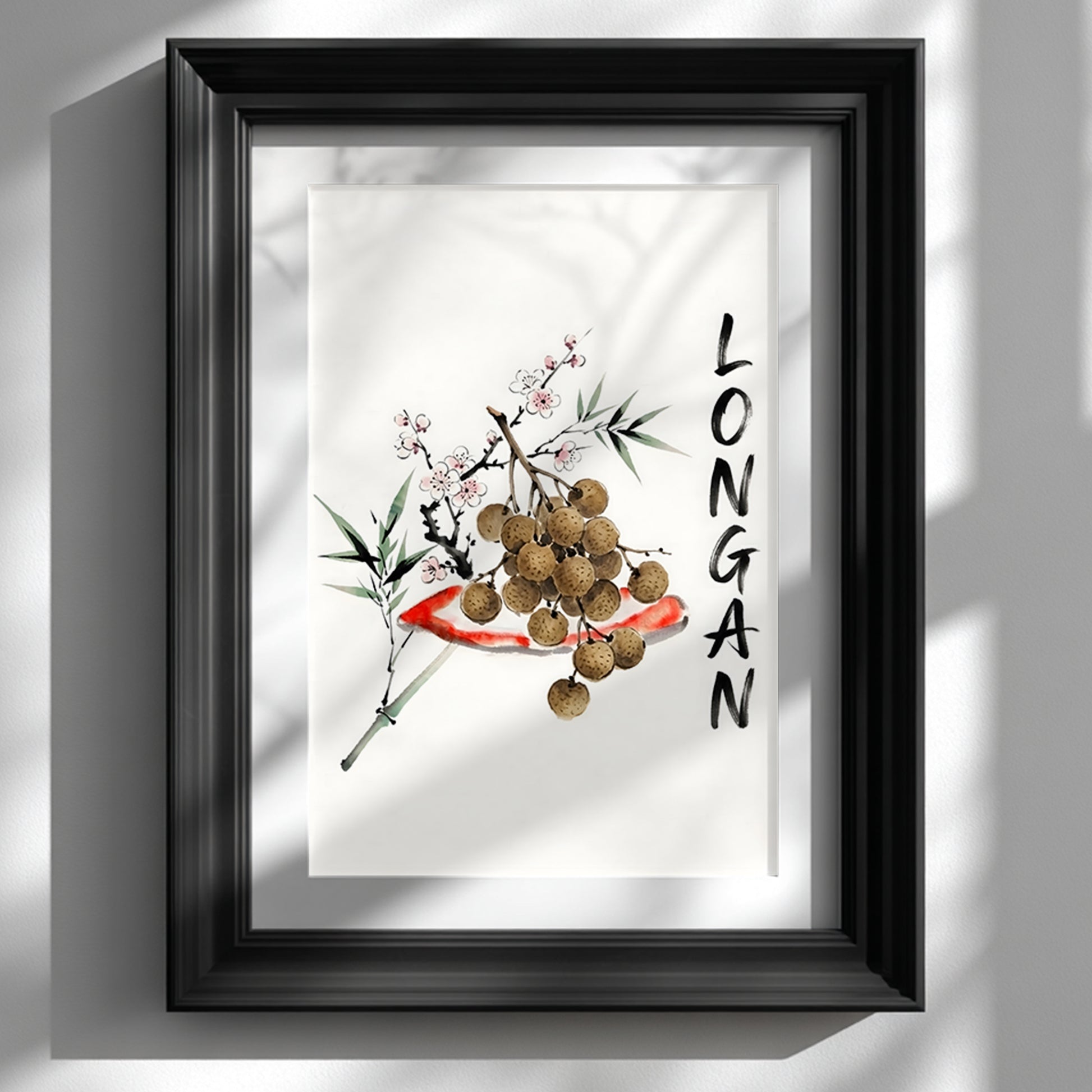 Black framed wall art print showing a minimalist Thai longan watercolour on a white wall. The artwork has brown longan fruit, green bamboo-style leaves, small blossom details and vertical black lettering, styled as Southeast Asia inspired fruit decor for kitchens, dining rooms or calm home interiors.