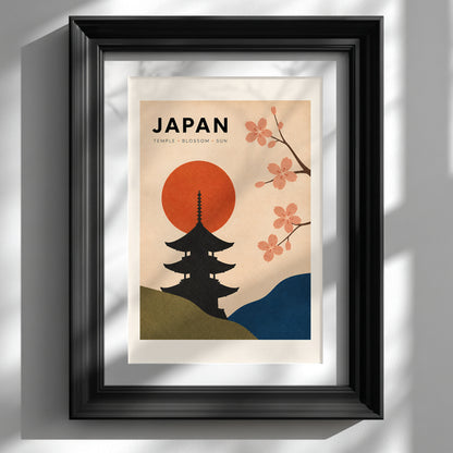 Vintage Japan travel poster shown in a deep black frame against a clean white wall. The artwork has a black Japanese temple silhouette, red rising sun, pink cherry blossom branches, olive green and blue hills, and a warm cream background, creating bold retro Asian wall art for a living room, bedroom or office.