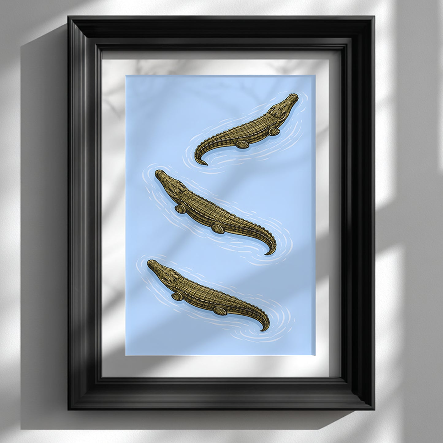 Black framed Triple Estuarine Crocodiles poster displayed against a bright white wall. Three saltwater crocodiles are arranged diagonally on a powder blue background, illustrated with detailed scales and ripple lines in a vintage natural history style. A minimalist reptile wall art piece suited to modern home decor, study rooms and contemporary gallery walls.