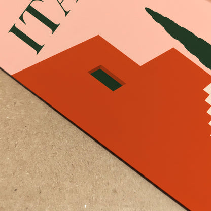Angled close-up of the Italia art print showing the crisp flat-colour design and physical print surface in detail. Terracotta architecture, a dark green window, cream stair shapes and part of the peach ITALIA heading are visible against a textured neutral background, highlighting the clean edges and bold mid-century composition.