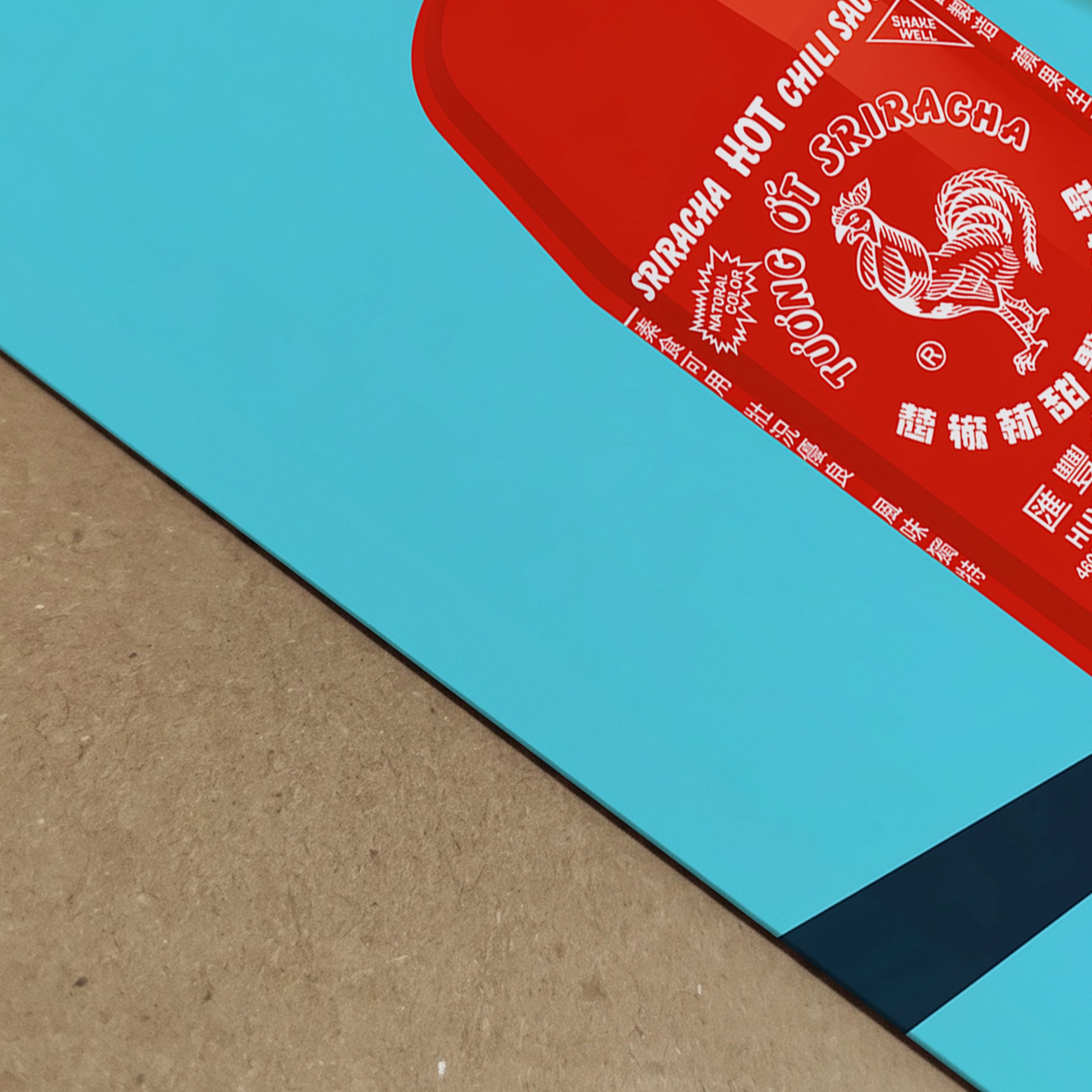 Close-up detail of the sriracha poster print, showing the red sauce bottle artwork, white label text, bright blue background, clean print edge and strong diagonal shadow. A bold pop art food print with colour depth and texture, made for kitchen decor, cafe wall art, restaurant styling or foodie interiors.