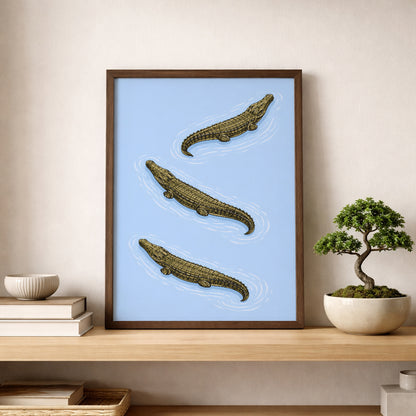 Triple Estuarine Crocodiles poster styled on a wooden shelf beside a bonsai tree and ceramic decor. The diagonal crocodile arrangement and blue background create a calm, specimen-like look. A natural history wildlife art print that suits study wall decor, minimalist interiors and reptile themed gallery wall styling.