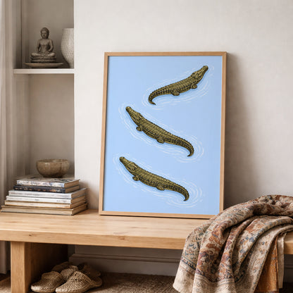 Crocodile wildlife poster displayed on a wooden shelf with folded textiles and neutral home accessories. The powder blue background highlights three saltwater crocodiles illustrated with detailed scales and ripple lines. A Southeast Asian inspired natural history print suitable for hallway decor, study rooms and modern animal art collections.
