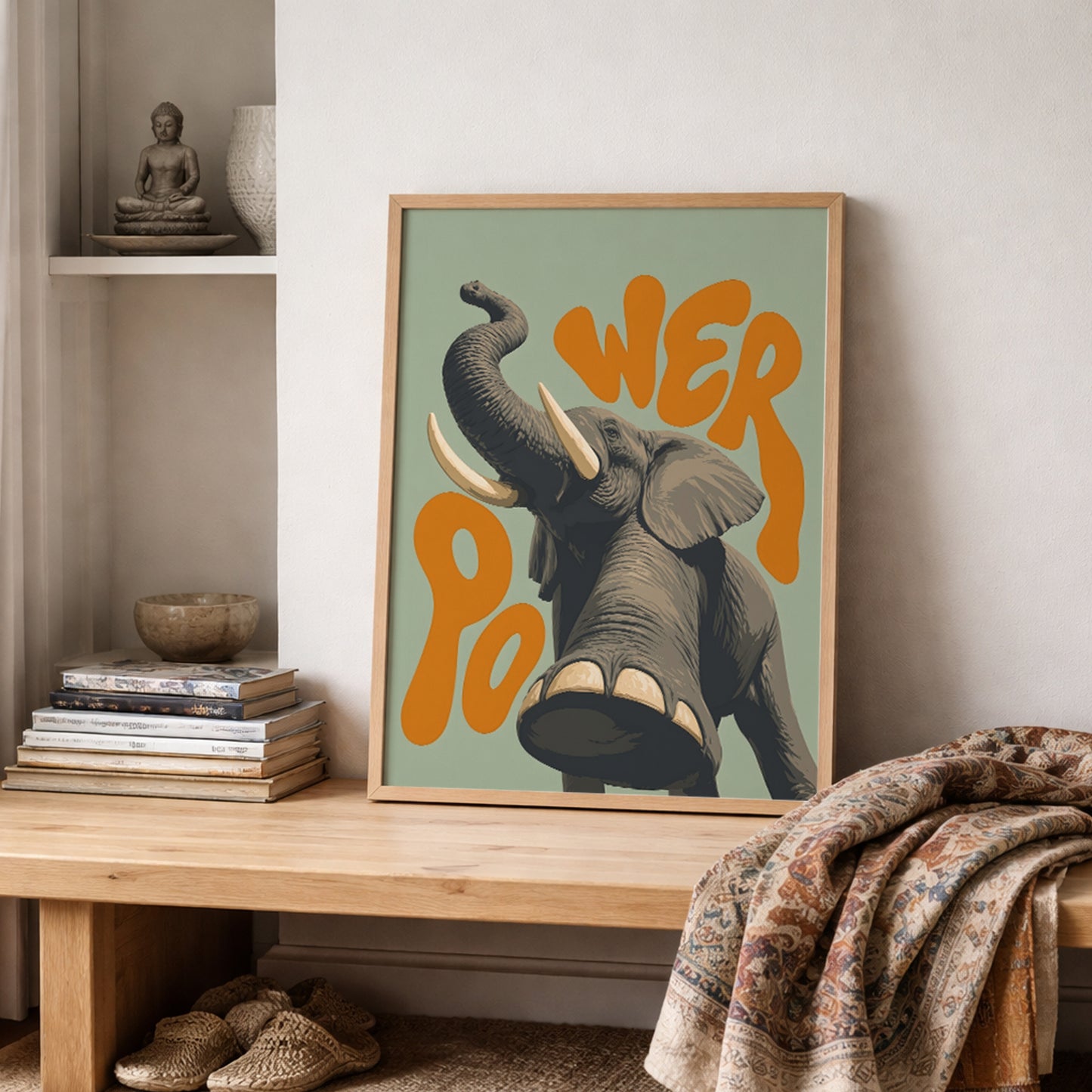 Framed elephant safari poster styled on a bedroom shelf with soft neutral bedding and textured home decor. The artwork shows a grey elephant with raised trunk, large tusks and orange retro lettering on a green background, making it a strong wildlife wall print for cosy bedrooms, kids’ rooms or relaxed home styling.