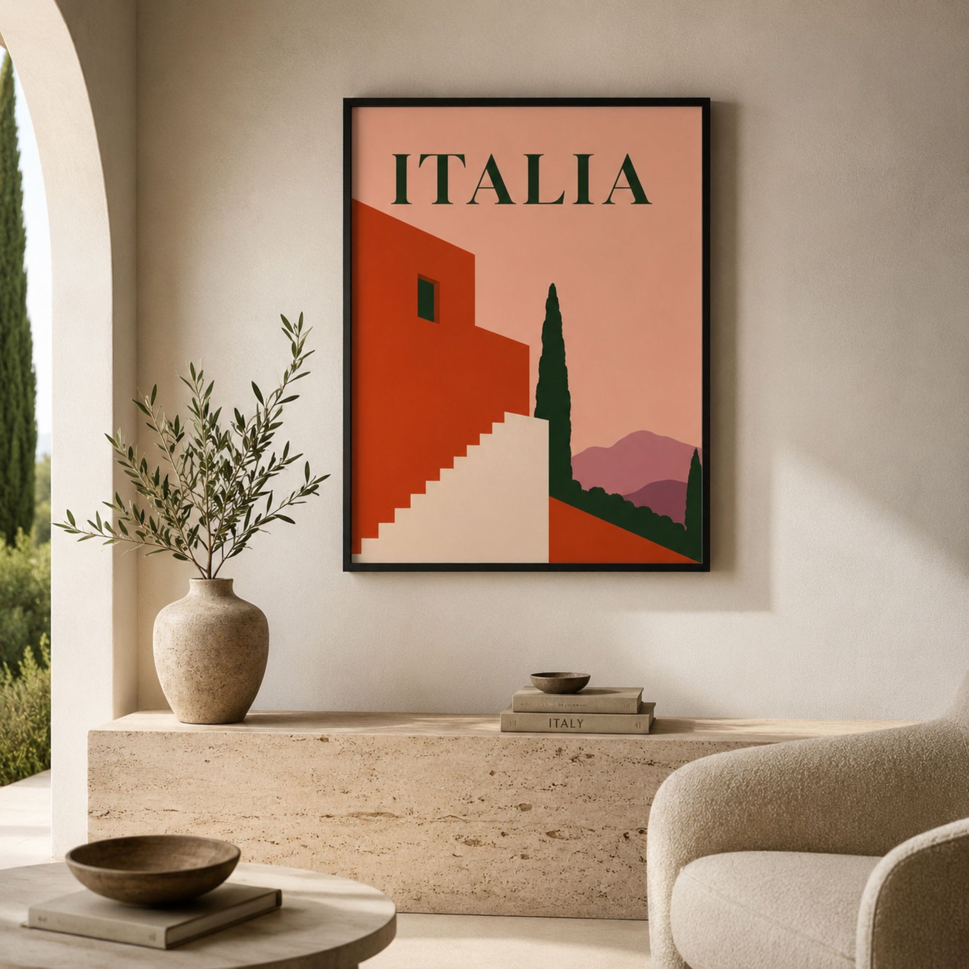 Framed Italian mid-century architecture print displayed in a calm neutral living room above a low cream sofa. The artwork features ITALIA lettering, a terracotta building, cream steps, dark green cypress tree and mauve hills, styled with a ceramic vase, soft furnishings and warm minimalist decor.