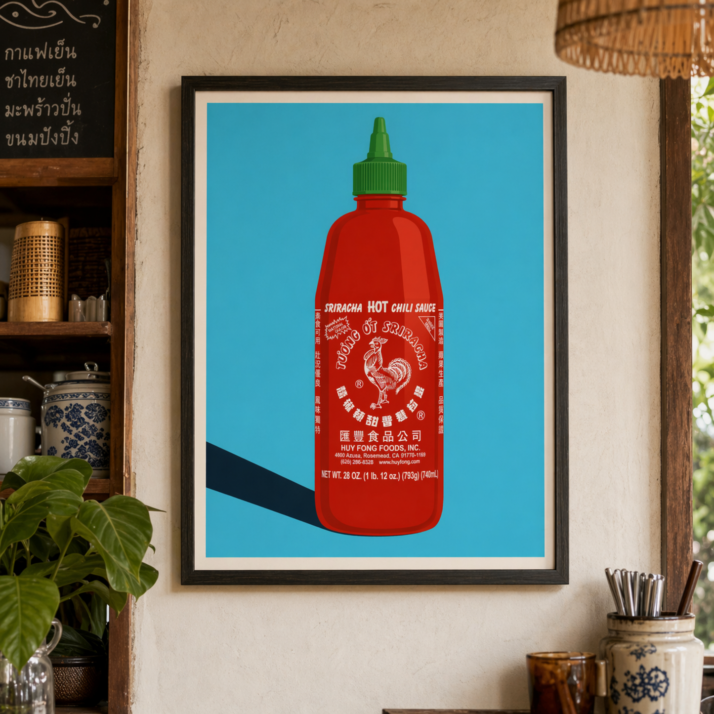 Framed sriracha poster styled in a kitchen shelf scene with plants, books and warm home decor. The artwork shows a red hot sauce bottle with green cap, white rooster logo and blue pop art background, making it a bold kitchen wall art print for food lovers, cafes, dining rooms or restaurant decor.