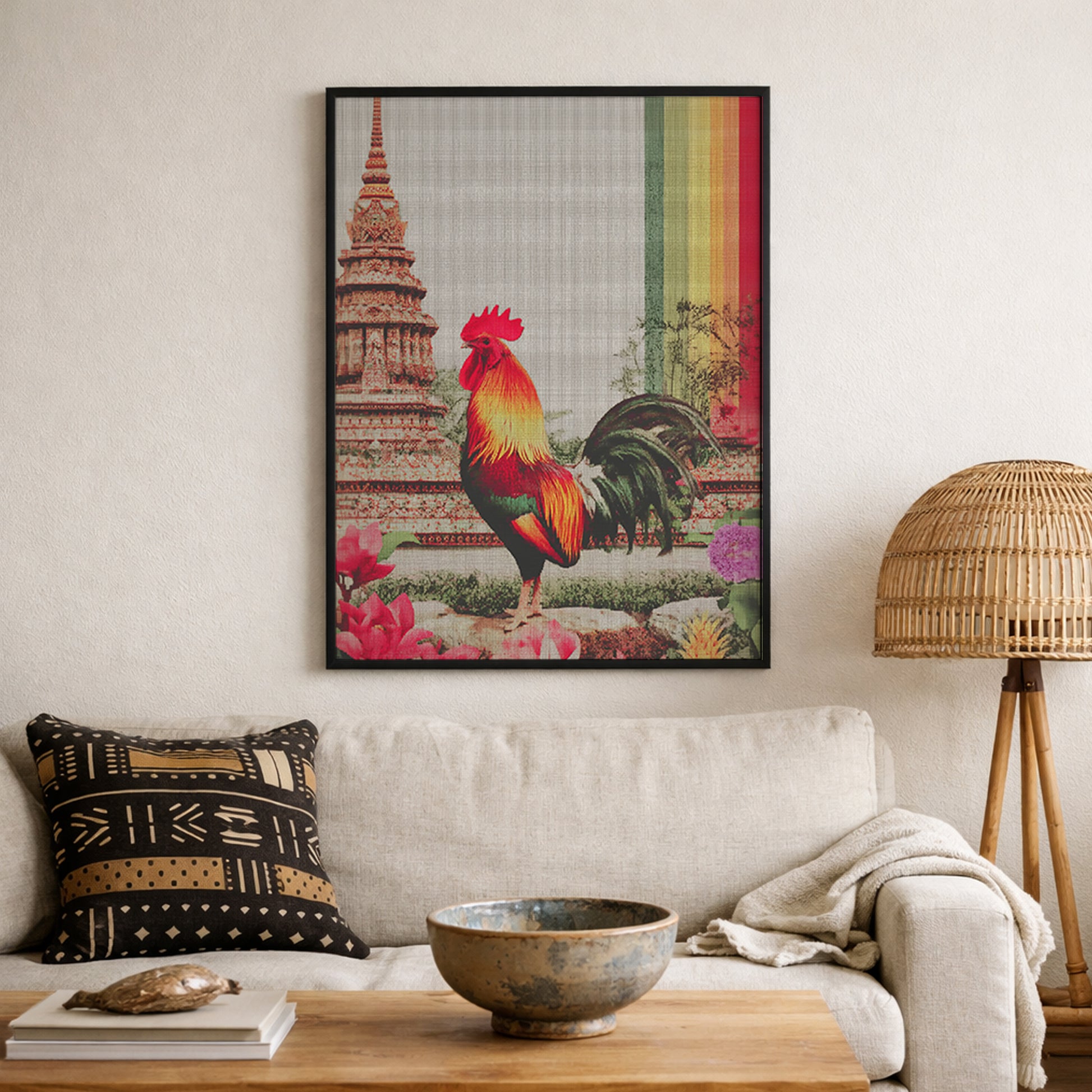 Framed Thai rooster wall art displayed above a sofa in a warm, textured living room. The artwork shows a vibrant rooster, temple architecture inspired by Wat Arun, clear canvas texture and a vertical multicolour rainbow stripe, complemented by woven baskets, plants and wooden furniture as statement cultural decor.