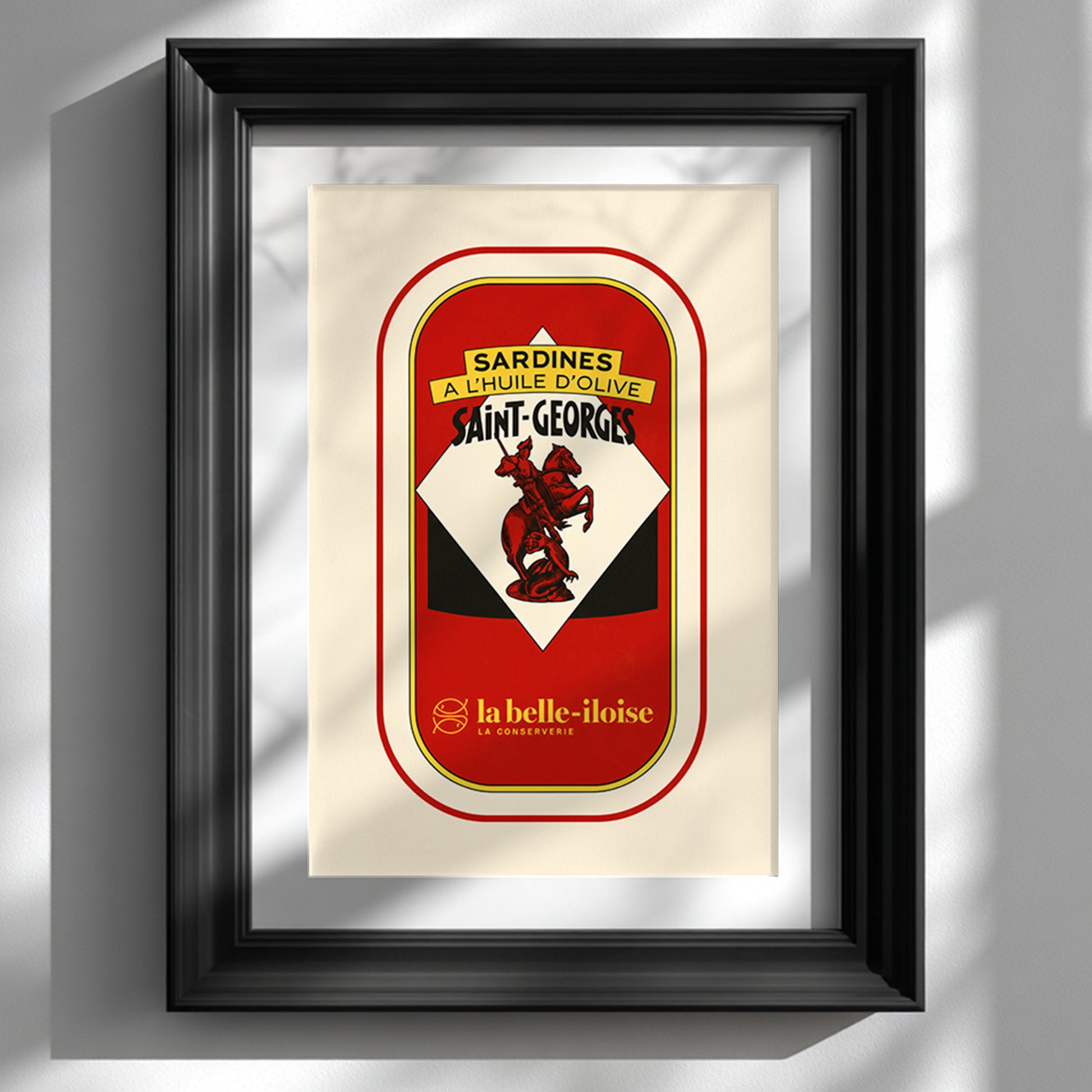 French sardine tin pop art print in a deep black frame on a white wall, with soft window shadows highlighting the red, cream, yellow and black vintage packaging design.