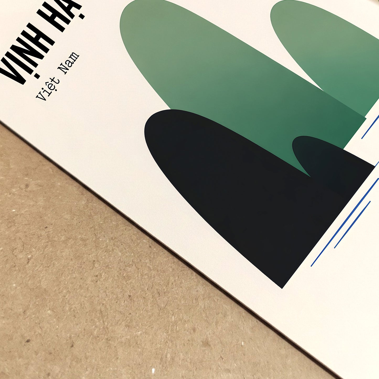 Angled close-up of the Ha Long Bay Vietnam poster laid on a light wooden surface, showing the printed paper, crisp edges and fine surface detail. The cropped view highlights the “Vinh Ha Long” title, layered green and black limestone shapes and clean blue water lines in this vintage-style travel print.
