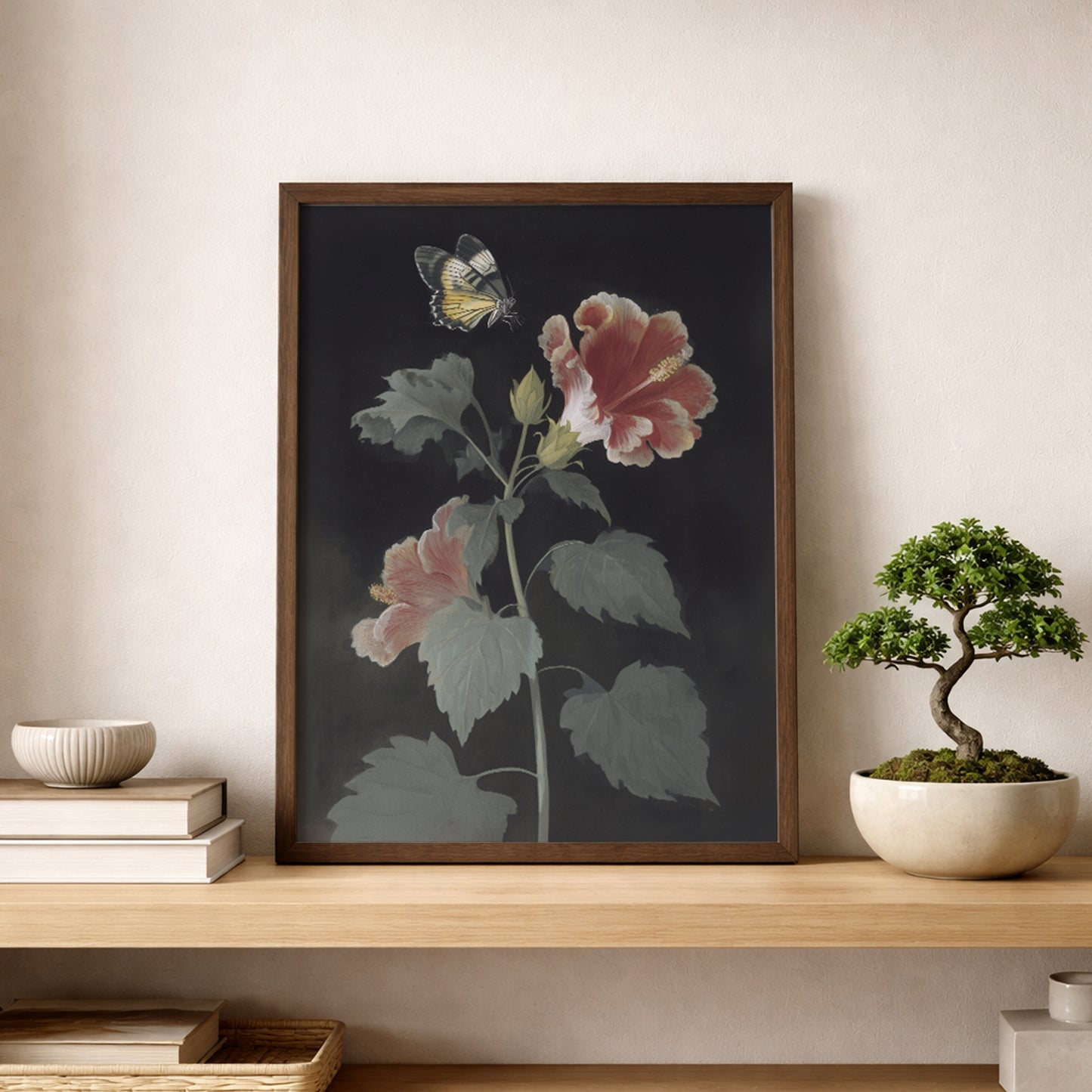 Malaysian hibiscus botanical poster placed on a wooden shelf beside a small bonsai tree and books. The artwork shows Bunga Raya flowers with red and pink petals and a Rajah Brooke’s Birdwing butterfly above. Tropical botanical wall art with a vintage feel styled in a minimal, nature-inspired shelf display.
