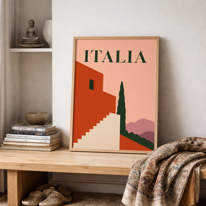 Italian mid-century poster displayed on a shelf beside folded woven textiles and simple neutral decor. The framed artwork shows bold ITALIA lettering, geometric terracotta buildings, a cream staircase, dark green cypress and soft mauve hills, adding warm travel-inspired colour to a bedroom, lounge or reading corner.
