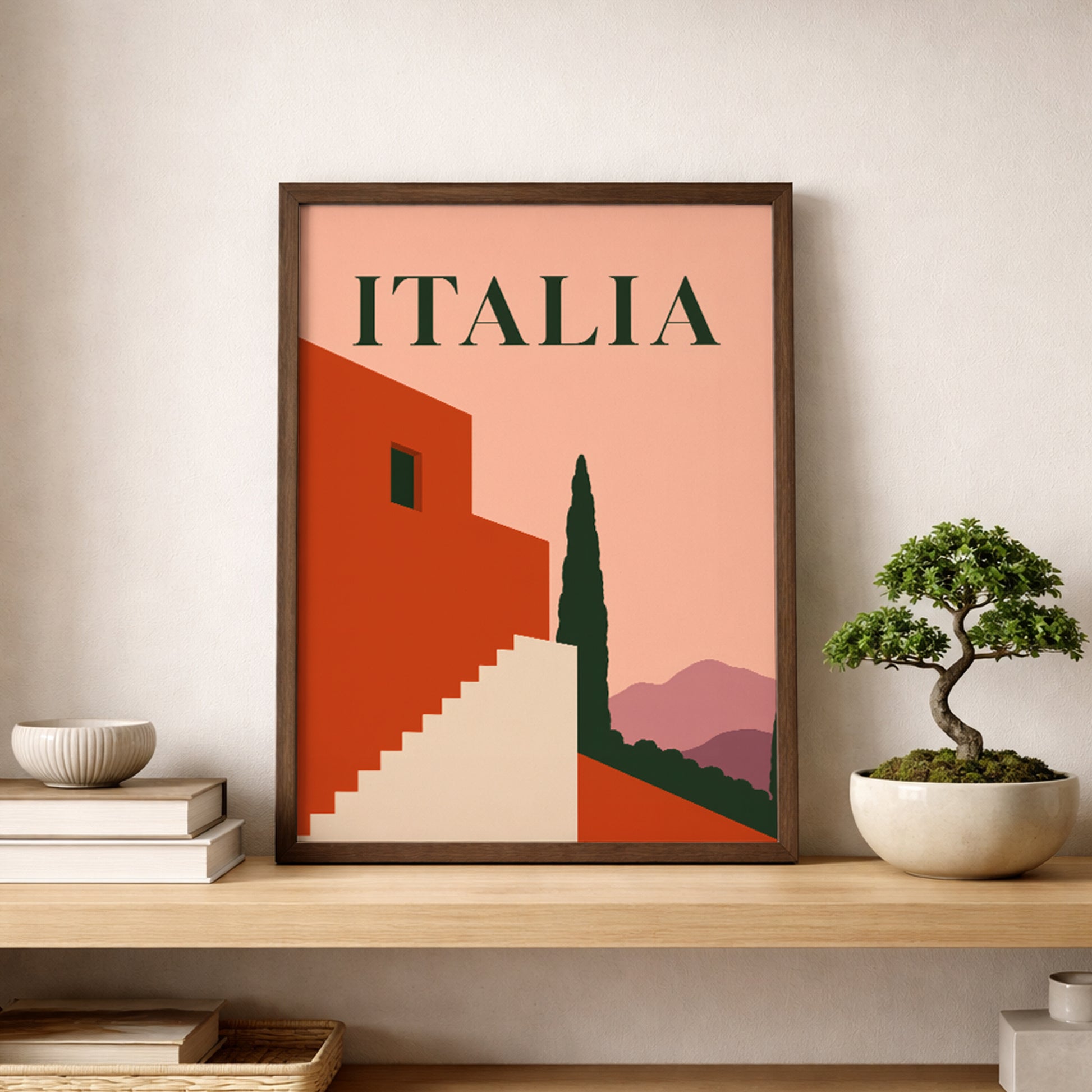 Framed Italia wall art resting on a light wooden shelf beside a small bonsai-style plant and neutral home accessories. The mid-century design combines a peach sky, terracotta architecture, cream stairs, dark green cypress tree and mauve hills, creating warm Mediterranean decor for a living room, hallway or study.