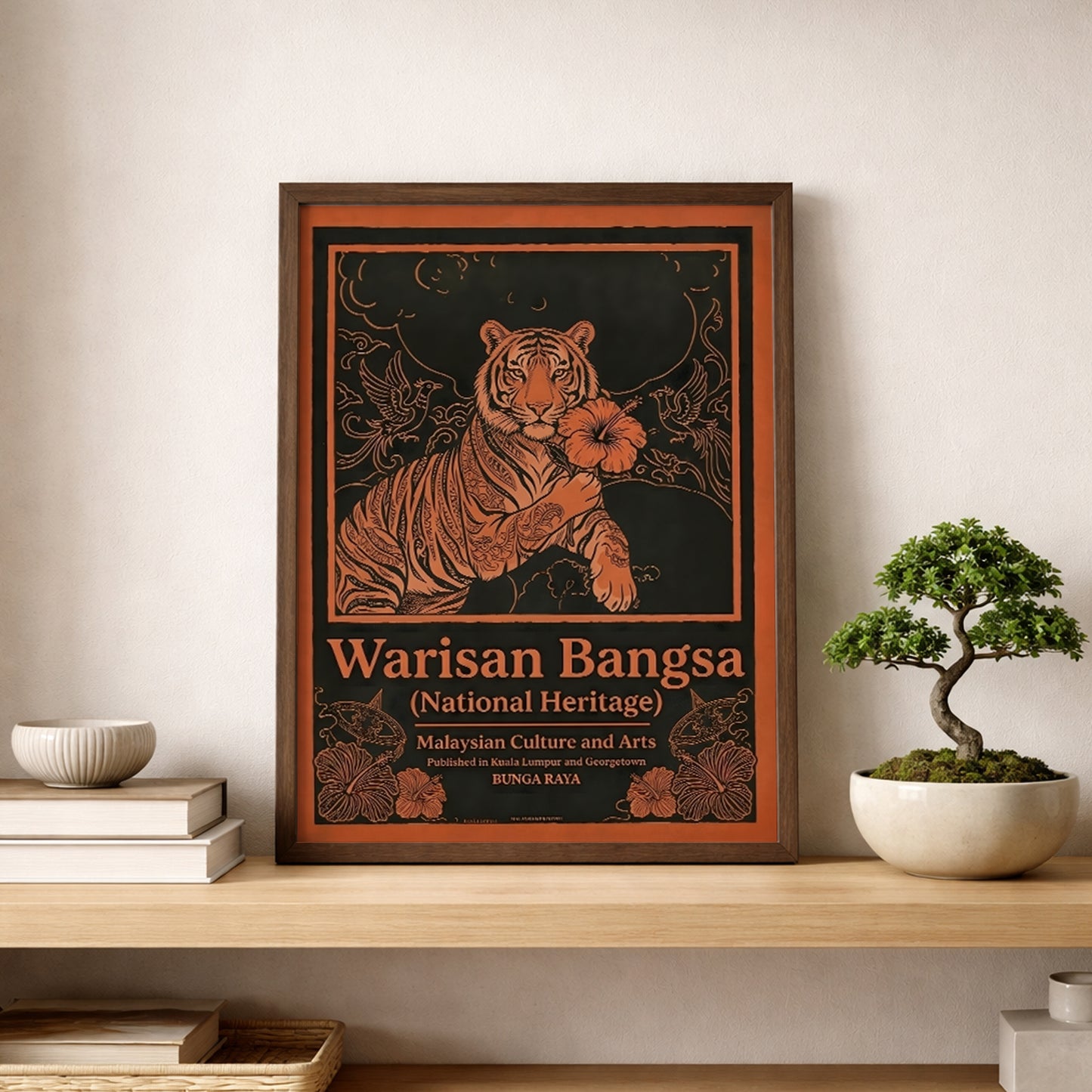 Malaysia poster Warisan Bangsa National Heritage leaning on a wooden shelf next to a small bonsai plant. The framed artwork shows a stylised tiger holding a hibiscus flower surrounded by birds and decorative floral patterns in bold orange linework on a dark background. Malaysian heritage wall art designed in a vintage poster style inspired by traditional decorative illustration.