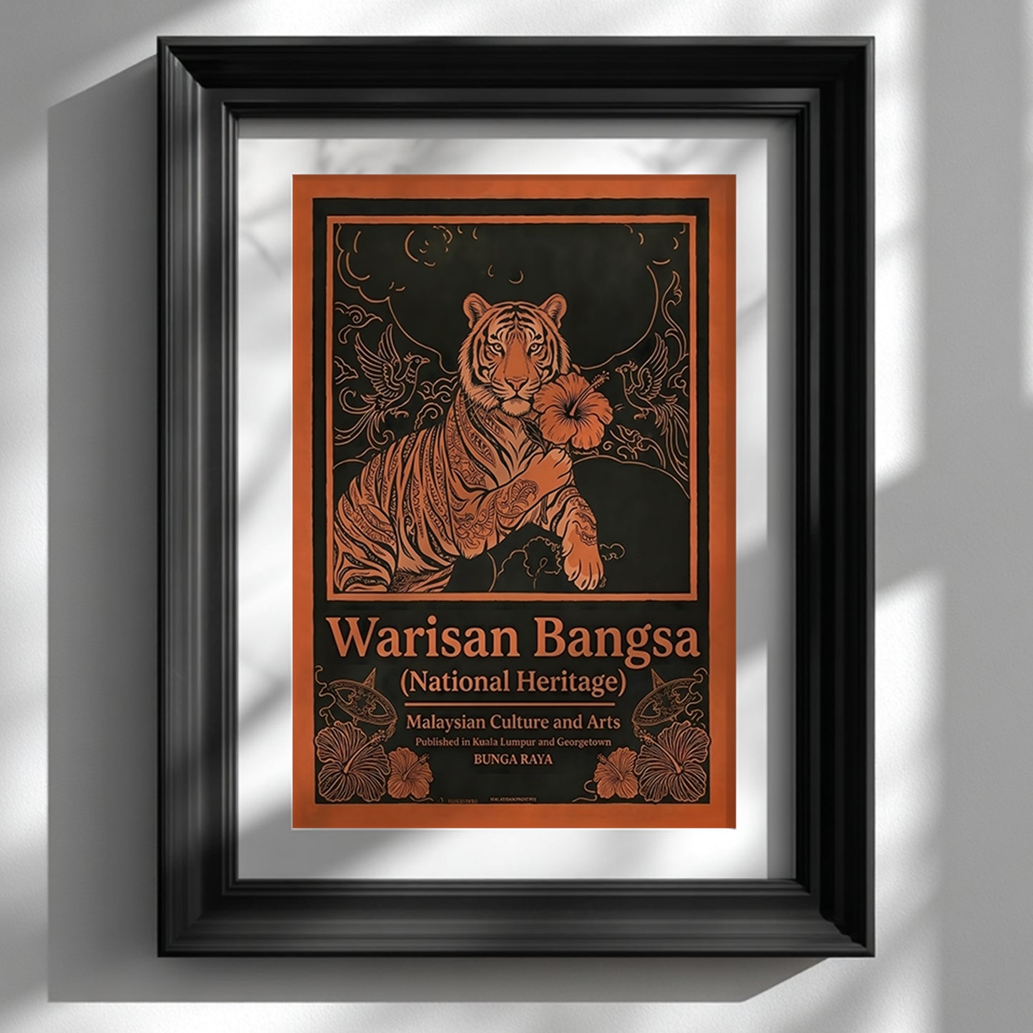 Framed Malaysia tiger wall art featuring the Warisan Bangsa National Heritage design displayed on a white wall in a black frame. The artwork shows a calm tiger holding a hibiscus flower (bunga raya) surrounded by decorative birds and floral patterns in bold orange linework on a dark background. A Malaysian culture poster styled as vintage graphic wall art representing national heritage and traditional illustration.