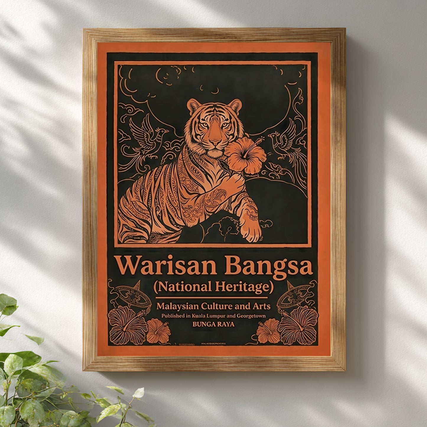Malaysia tiger wall art Warisan Bangsa National Heritage displayed in a wooden frame on a neutral white wall. The poster features a stylised tiger holding a hibiscus flower with surrounding birds and decorative floral lines illustrated in bold orange against a dark background. Malaysian heritage poster design inspired by traditional culture and vintage decorative illustration.