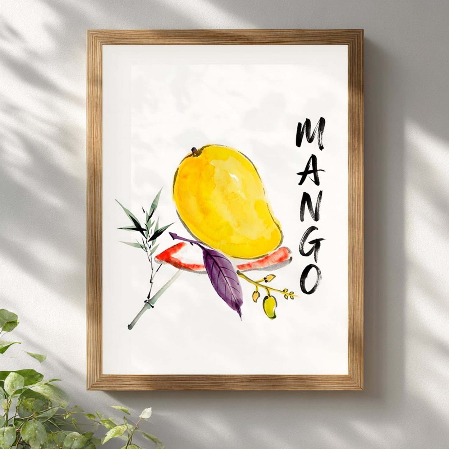 Mango watercolour wall art displayed in a light wood frame on a white wall with soft natural shadows. The artwork features a yellow mango, loose botanical brushwork, green and purple leaves, a small fruit branch and bold vertical MANGO text on a white background. The clean framed presentation suits kitchen wall art, fruit wall decor, tropical fruit print styling or modern botanical interiors with a light, simple feel.