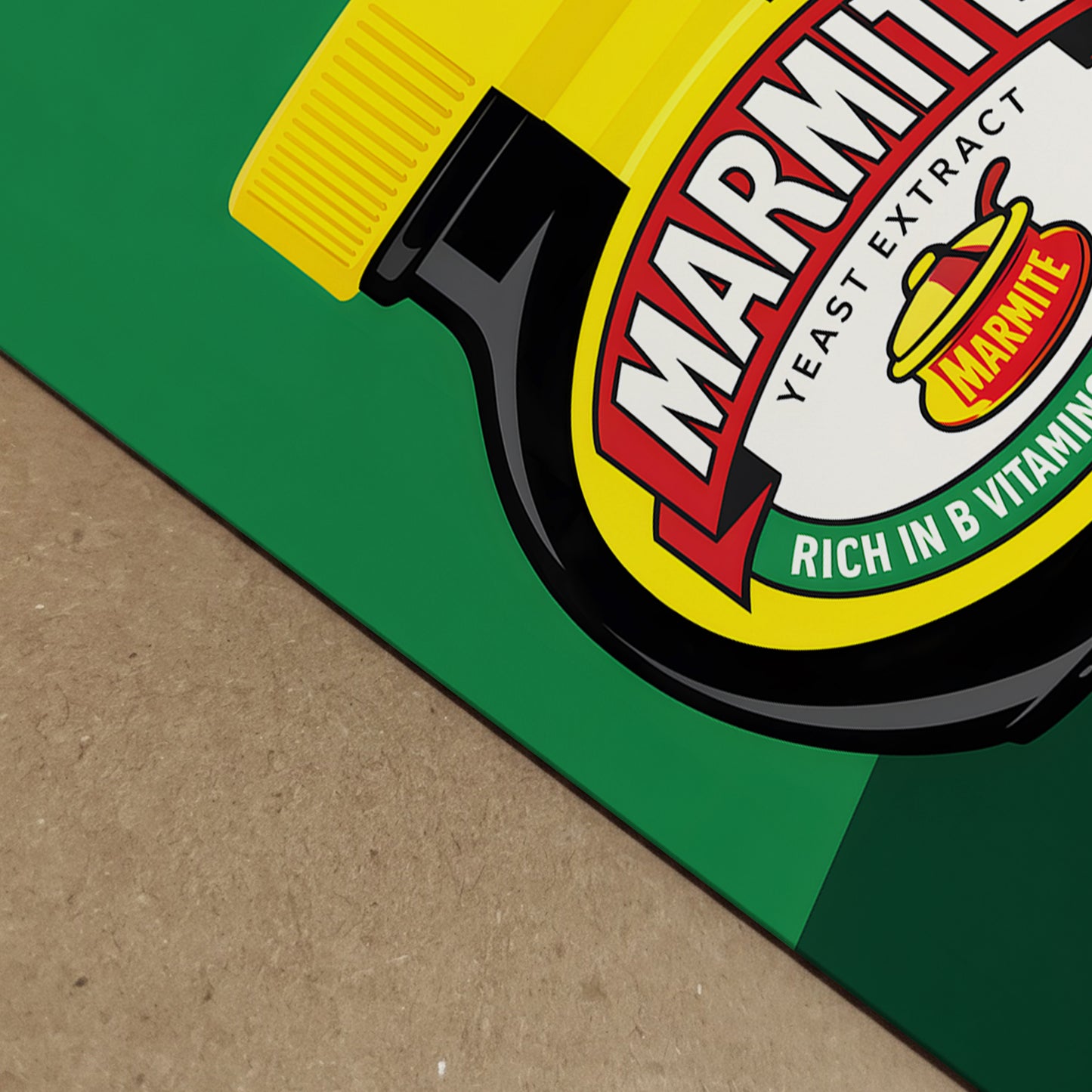 Angled close-up of the Marmite Jar Print showing the lower corner of the artwork and part of the jar label in sharp detail. The image highlights the smooth print surface, bold green background, black jar edge and yellow lid, with shallow depth for a more realistic product view. Useful for showing the crisp graphic finish of this marmite pop art piece and modern British food-inspired wall art.