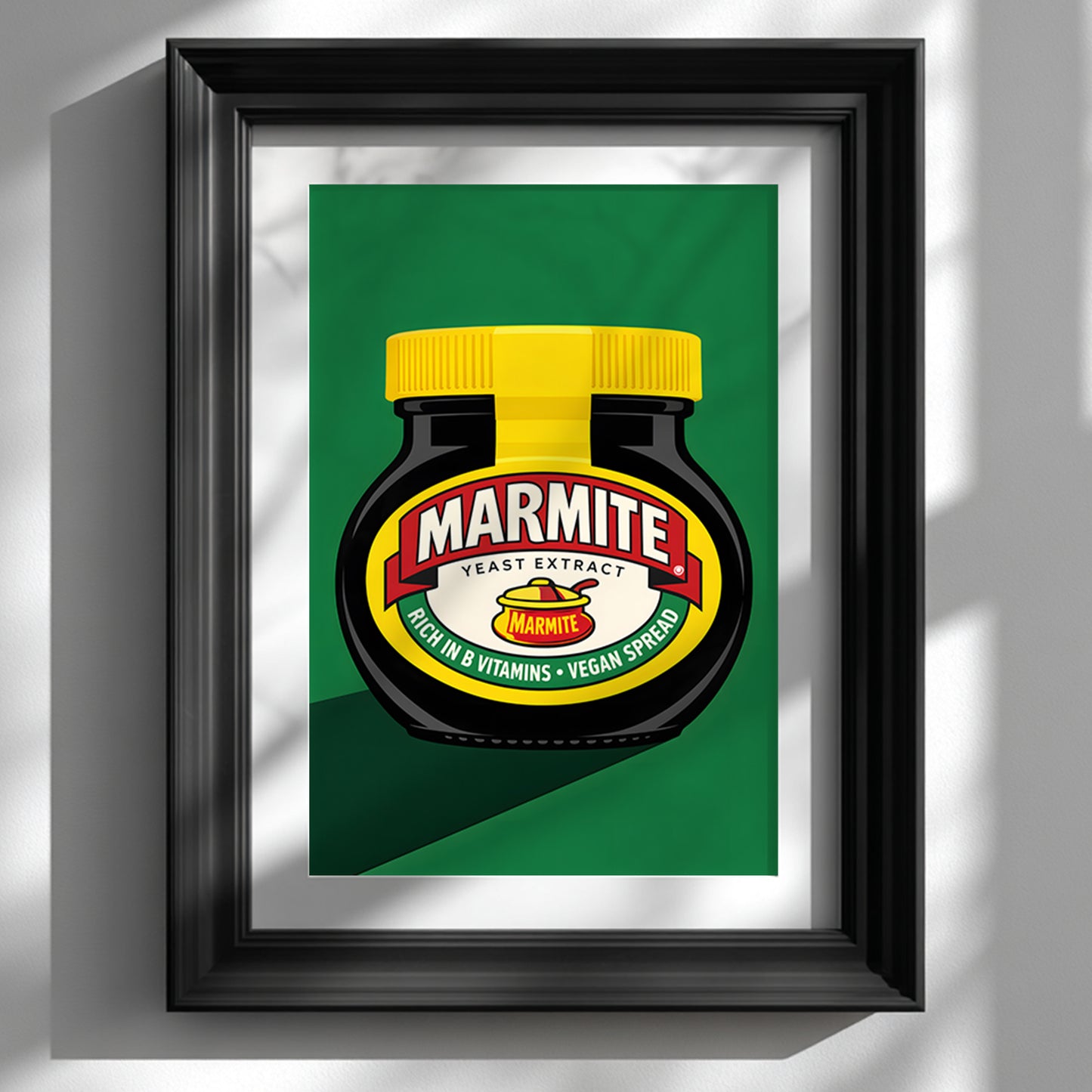 Framed Marmite Jar Print shown on a white wall in a glossy black frame with a wide white mount. The artwork features a black Marmite jar with a bright yellow lid, red and cream label, and green background in a bold pop art style. Clean lines, strong contrast and simple modern styling make it ideal for British kitchen wall art, contemporary food art and framed dining room decor.