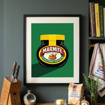 Marmite Jar Print styled in a home kitchen setting with the artwork framed against a dark wall beside shelves, books and food items. The print shows a black Marmite jar with a yellow lid on a green background, echoing classic British pantry colours. The scene gives a lived-in, casual look that suits British kitchen decor, food-themed wall art and playful modern dining space styling.