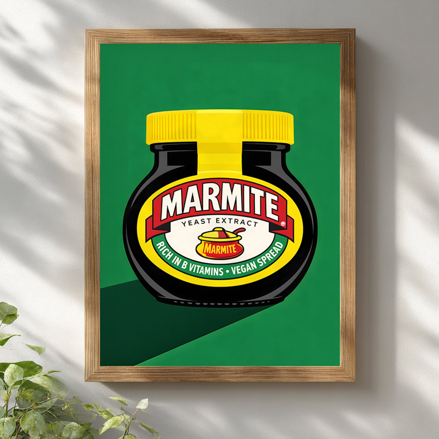 Marmite Jar Print displayed in a light wooden frame on a white wall with soft natural shadows. The artwork shows a black Marmite jar with a bright yellow lid, red and cream label, and green background in a clean graphic style. The lighter frame gives it a softer look while keeping the bold British food theme, making it suitable for contemporary kitchen decor and modern dining wall art.