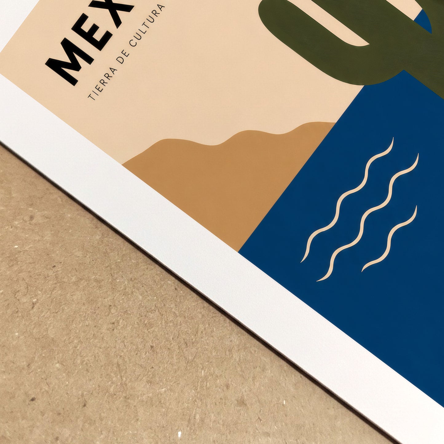  Close-up angled view of the Mexico art print lying on a textured neutral surface, showing the crisp white paper edge and detailed printed colours. The crop highlights the cream background, blue sea, green cactus and flowing linework, giving a clear view of the poster’s paper finish and print quality.