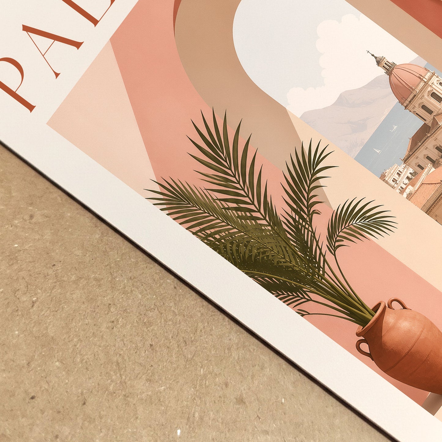 Close-up view of a Palermo Italy travel poster lying on a textured neutral surface, showing the printed paper edge and detailed artwork. The composition highlights the peach archway, terracotta plant pot, green palm leaves and sunlit Sicilian architecture. A realistic product detail image for Mediterranean art prints and Italian wall decor.