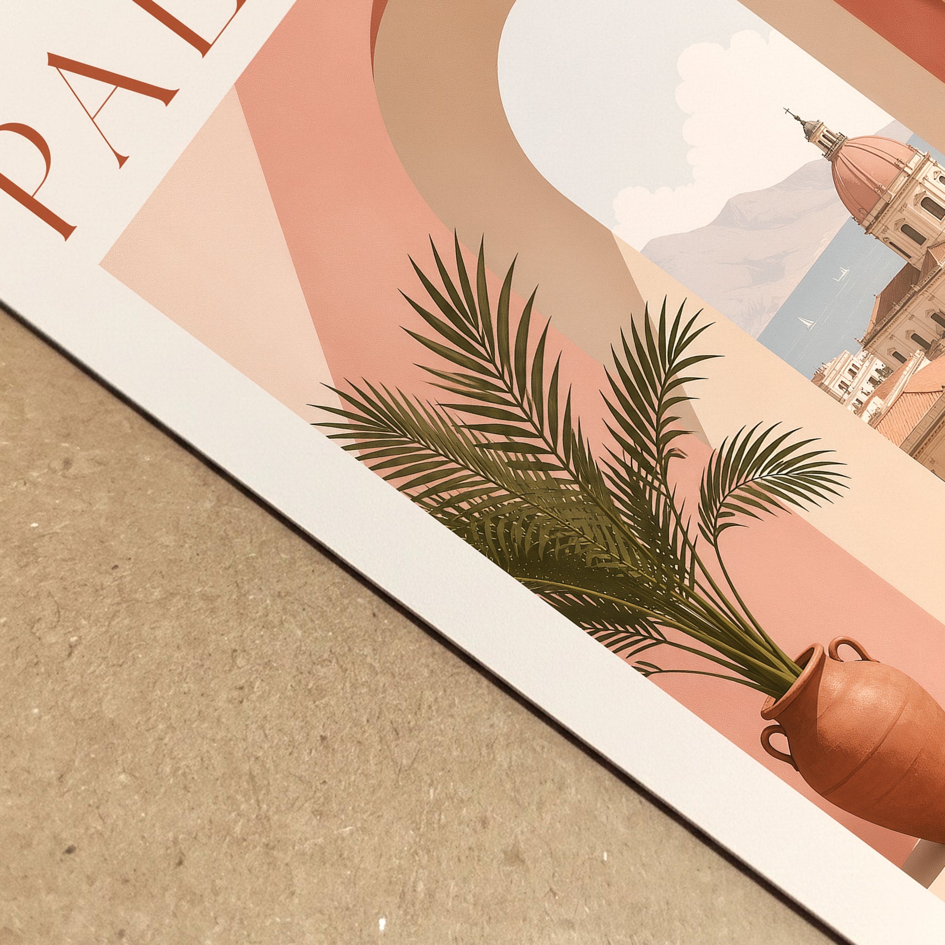 Close-up view of a Palermo Italy travel poster lying on a textured neutral surface, showing the printed paper edge and detailed artwork. The composition highlights the peach archway, terracotta plant pot, green palm leaves and sunlit Sicilian architecture. A realistic product detail image for Mediterranean art prints and Italian wall decor.