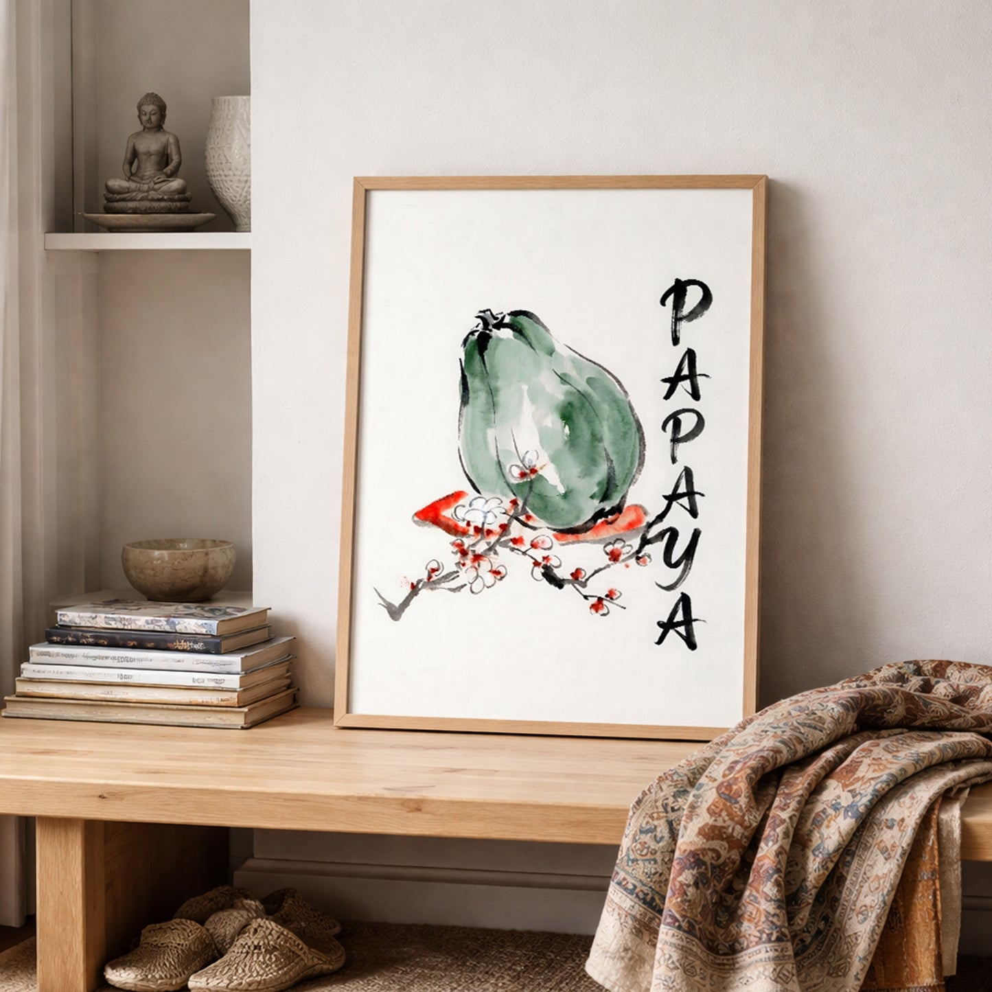 Papaya art print styled on a wooden shelf with books, ceramics, and folded fabric in a calm neutral room. The framed artwork features a green papaya, loose black brushwork, red and white blossom accents, and vertical PAPAYA lettering. Ideal lifestyle mockup for fruit wall art, papaya poster, kitchen decor, tropical botanical styling, and simple modern interiors.