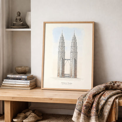 Petronas Towers architectural line art poster framed and styled on a wooden shelf with stacked books and textiles. The Kuala Lumpur Twin Towers are illustrated symmetrically with the connecting sky bridge and subtle sky background, forming minimalist Malaysia architecture wall art designed for modern interior decor.