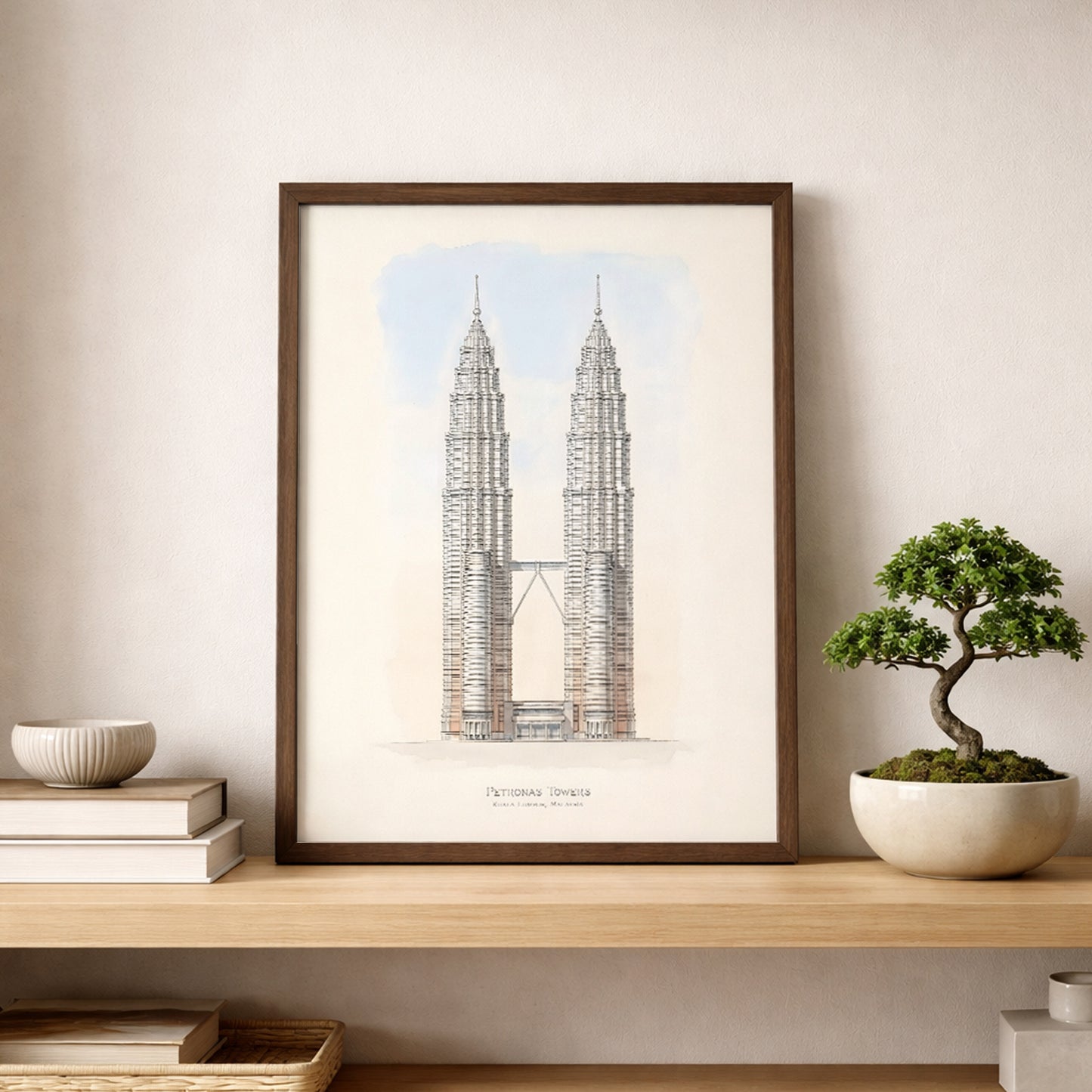 Framed Petronas Towers architectural line art print displayed on a wooden shelf beside a bonsai plant and ceramic decor. The minimalist Kuala Lumpur skyline artwork features the symmetrical Twin Towers and sky bridge with soft sky tones, creating modern Malaysia architecture wall art suited to calm, contemporary interiors.