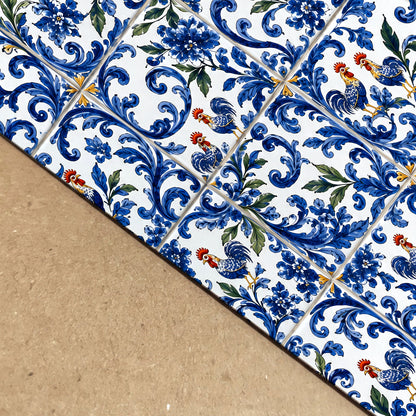 Close-up view of a Portuguese azulejo print showing detailed blue floral tile patterns, green foliage and colourful rooster motifs printed on paper against a warm neutral surface.