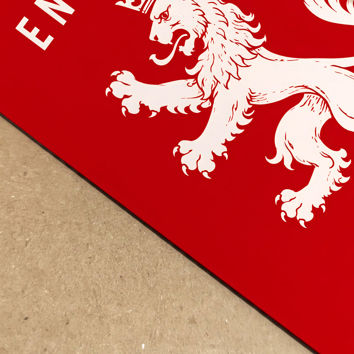 A close-up of a red rectangular product, likely a mat or board, featuring a white lion rampant graphic and partial white lettering, placed on a tan textured surface.