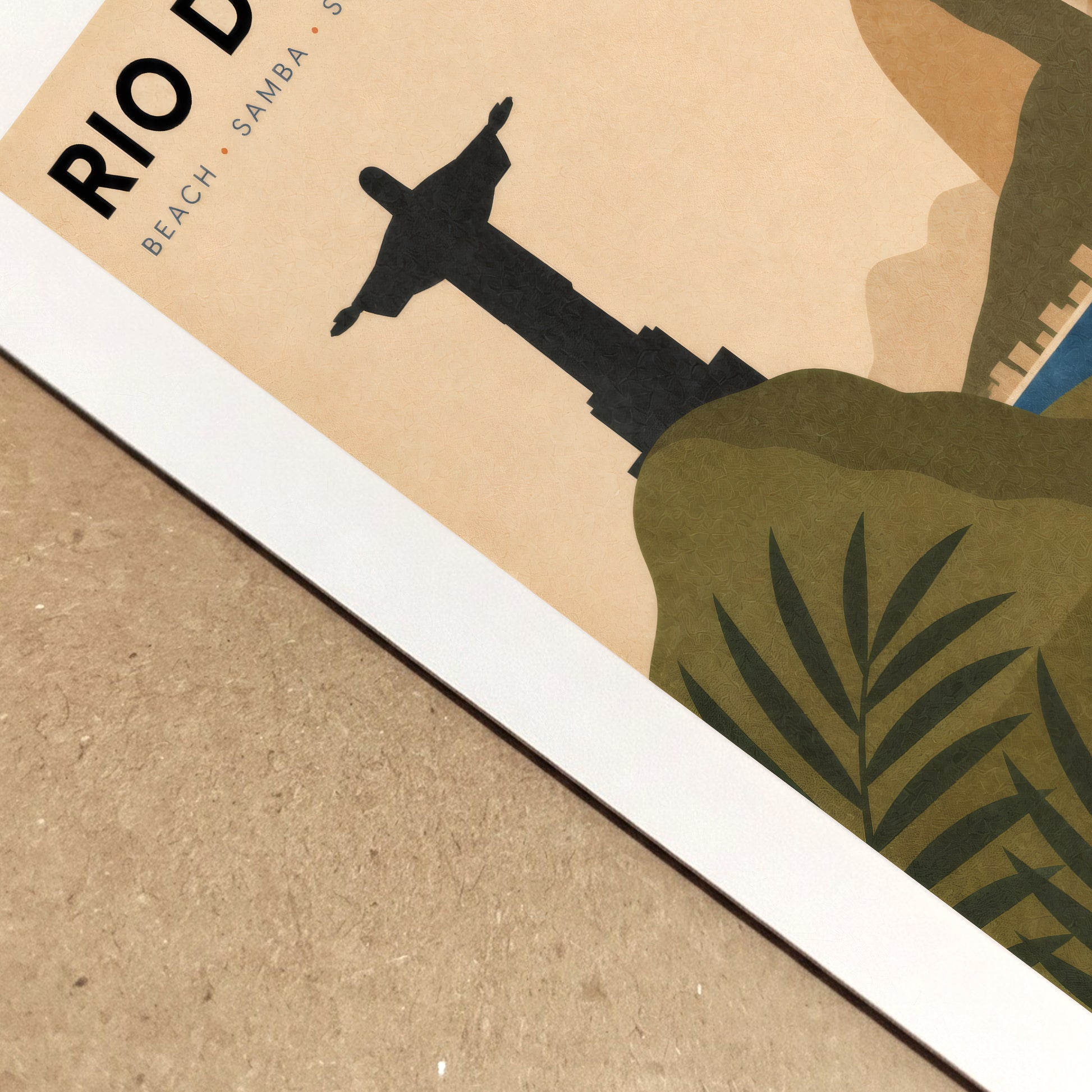 Close-up view of the Rio de Janeiro travel poster lying on a textured neutral surface, showing the paper edge, printed colours and fine surface detail. The cropped design includes Christ the Redeemer, tropical foliage, blue coastline and warm retro shades, highlighting the quality of the Brazil art print.